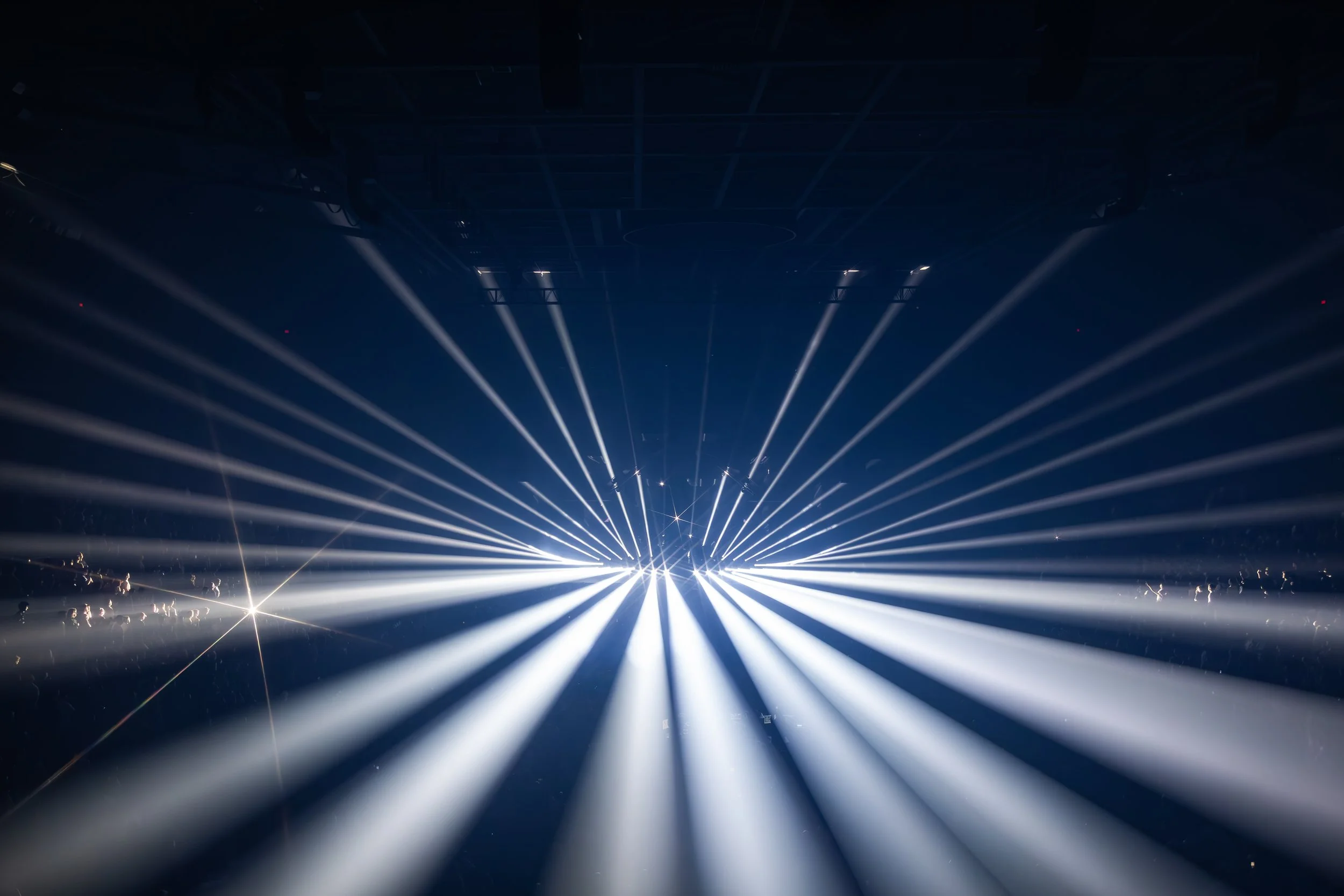 Jeux de lumières avec des rayons lumineux blancs émanant d'une source centrale dans une ambiance sombre, probablement à un concert ou un événement lumineux.