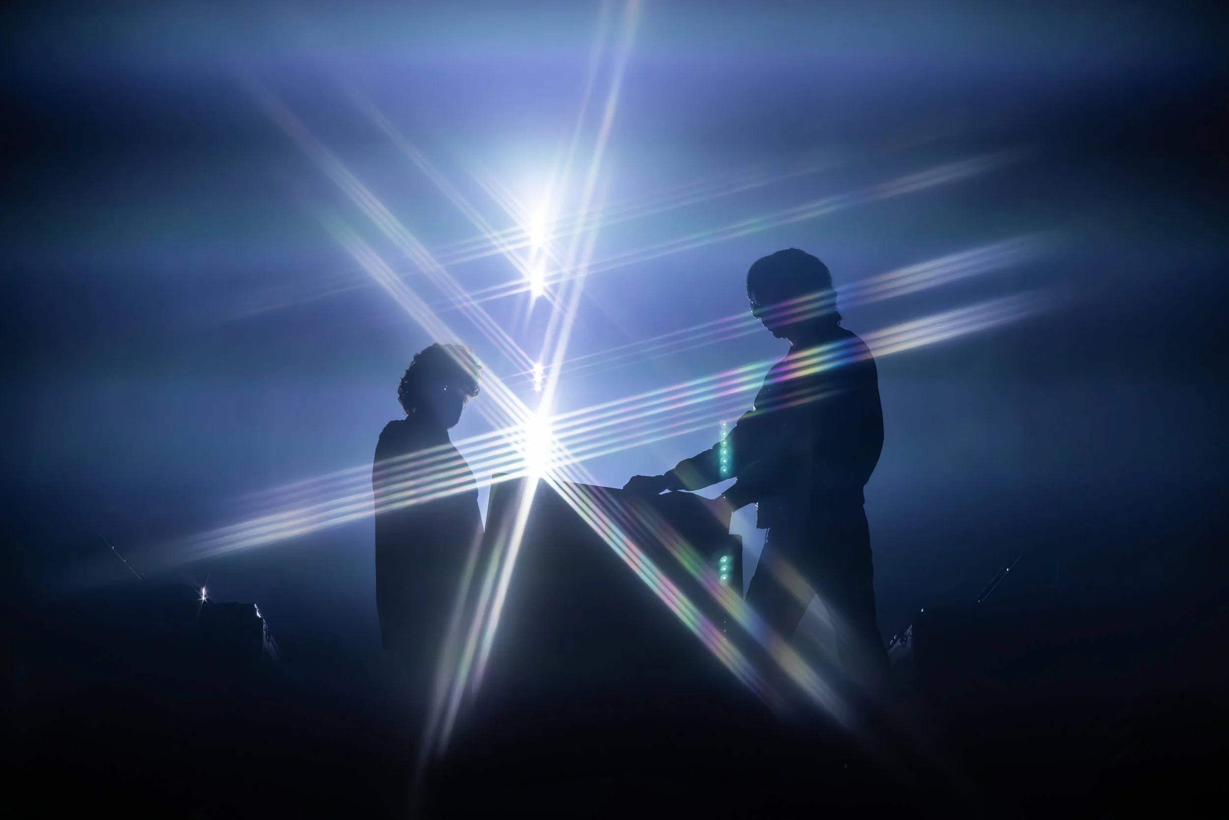 Silhouettes de deux personnes dans un éclairage brillant avec des lignes lumineuses multicolores.