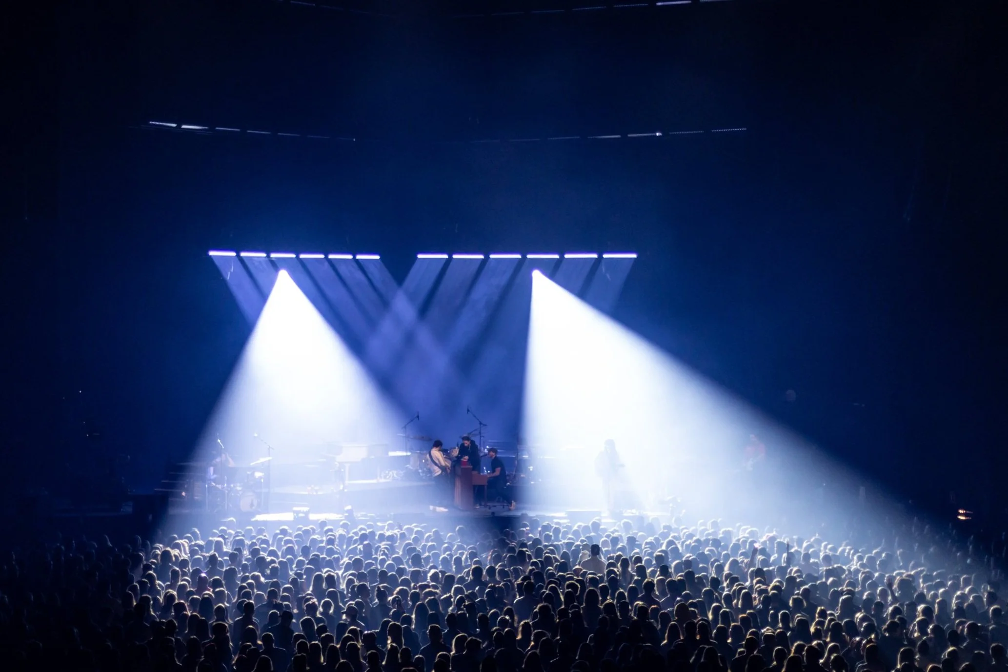Spectacle de lumière et un groupe de musiciens sur scène devant une grande foule dans une salle de concert