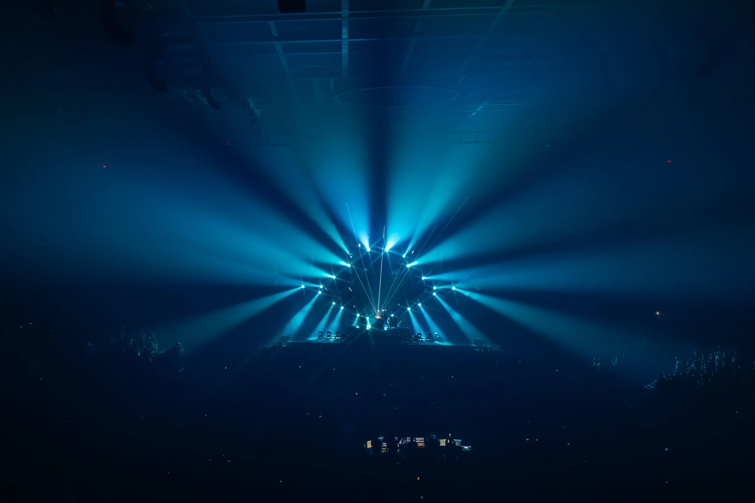 Scène d'un concert ou d'un spectacle avec des jeux de lumières bleues concentrés sur une scène vide, dans une grande salle.