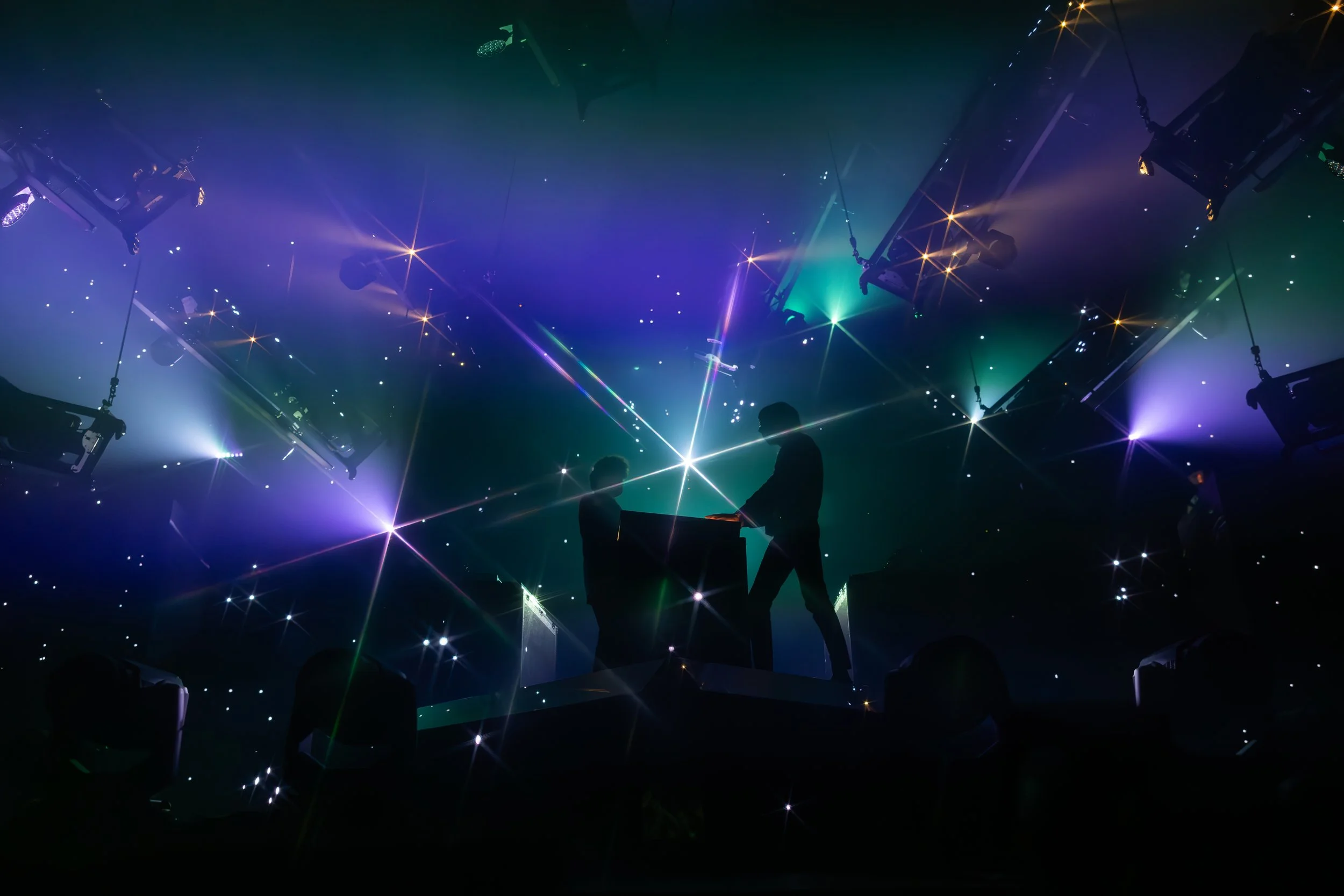 Deux personnes jouant du piano sur scène sous des lumières colorées et des effets de laser, dans un spectacle lumineux.