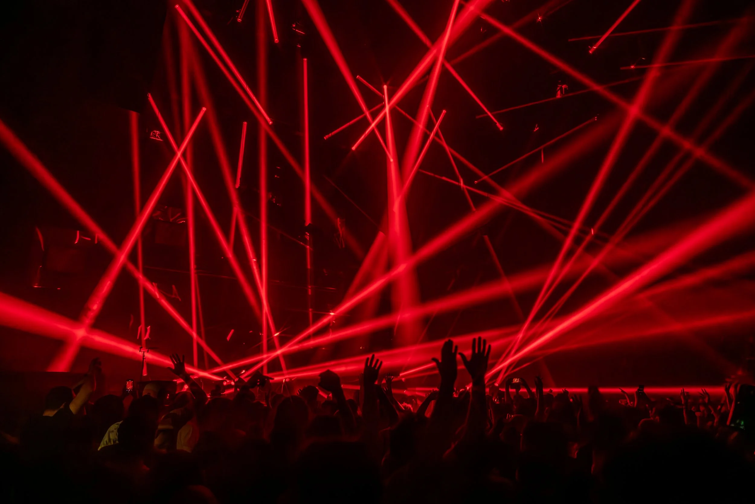 Spectacle de feu et de lumières avec des rayons laser rouges illuminant une foule de spectateurs lors d'un concert ou d'un événement en intérieur.