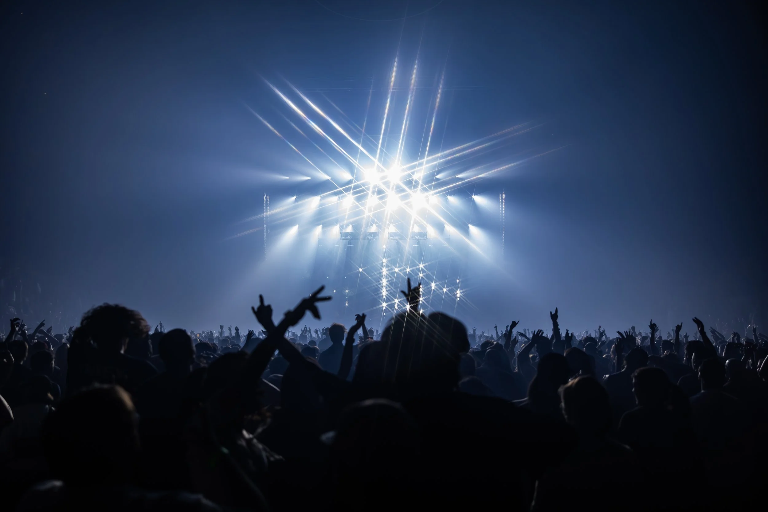 Une foule de personnes assistent à un concert ou un festival avec un éclairage intense et des rayons lumineux bleus.