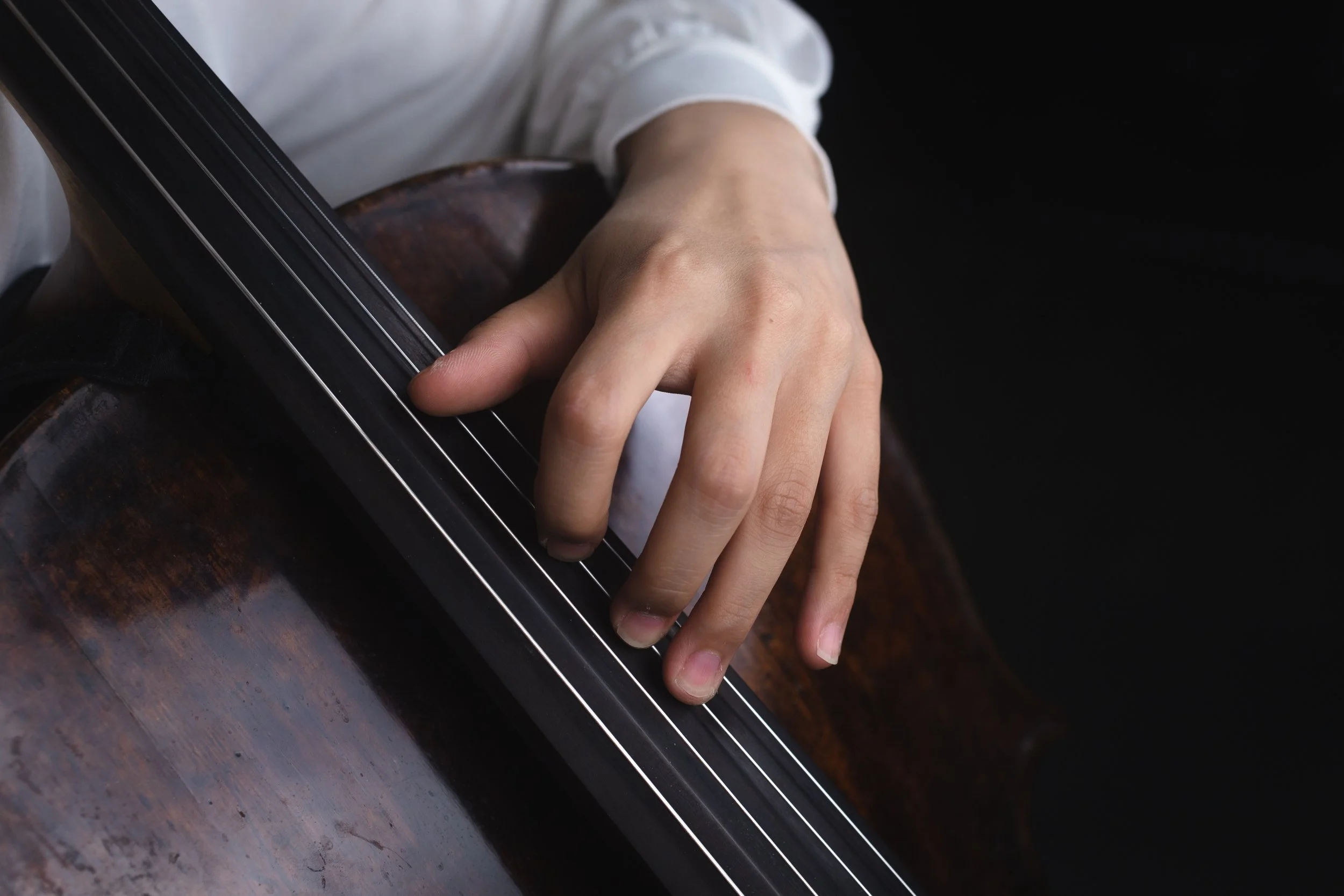 Close-up of a person's hand playing a cello, focusing on fingers pressing the strings.