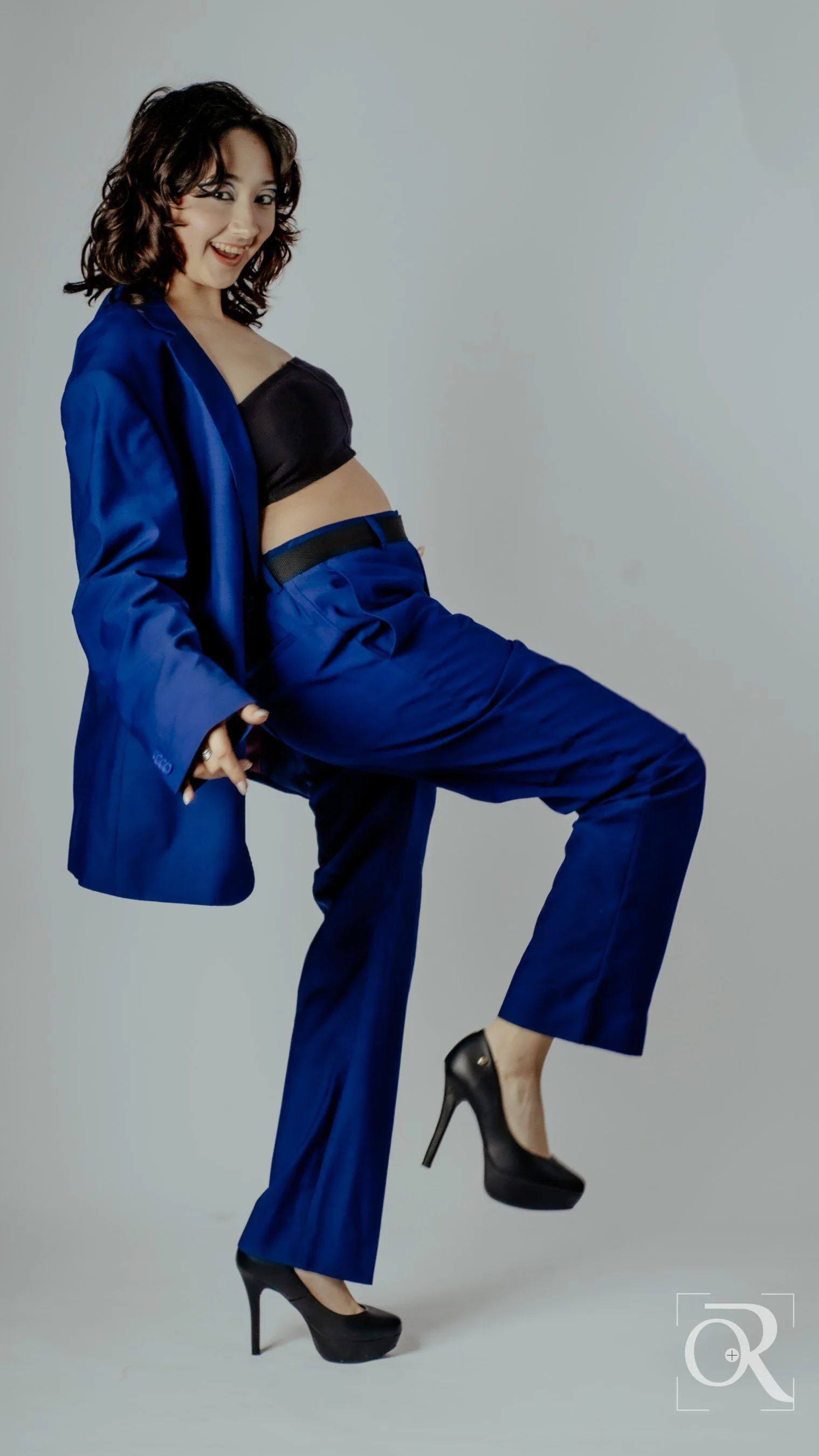 Mujer posando con ropa de vestir azul y tacones negros, con una expresión alegre y en una postura elegante.