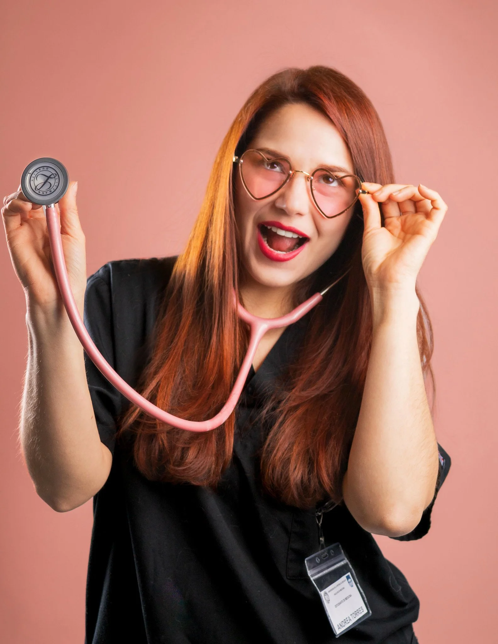 Enfermera jovial con gafas de corazón, sosteniendo un estetoscopio rosa, con fondo rosa