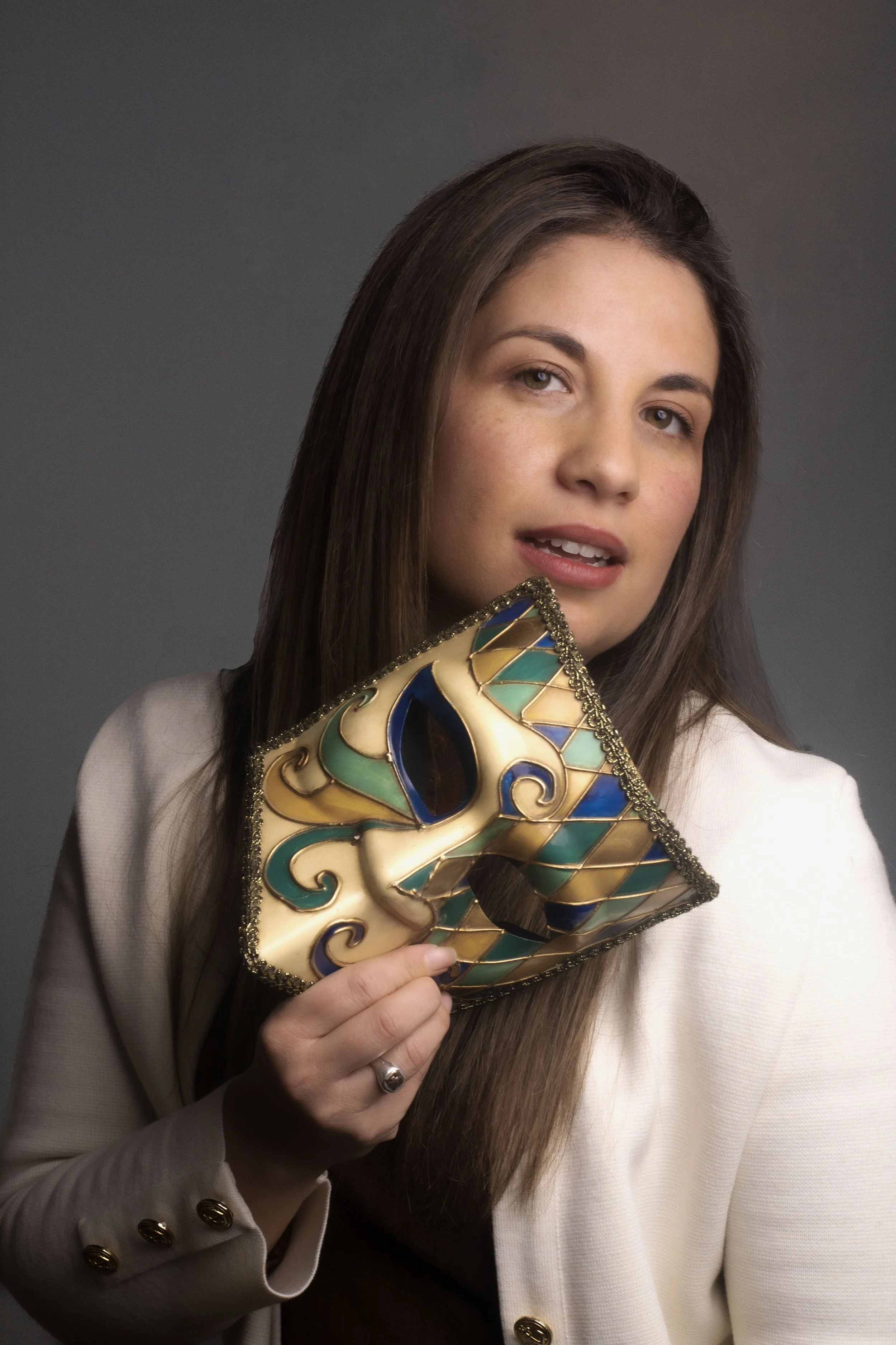 Mujer con cabello largo y liso, sosteniendo una máscara de carnaval decorada con detalles en azul, verde y dorado.