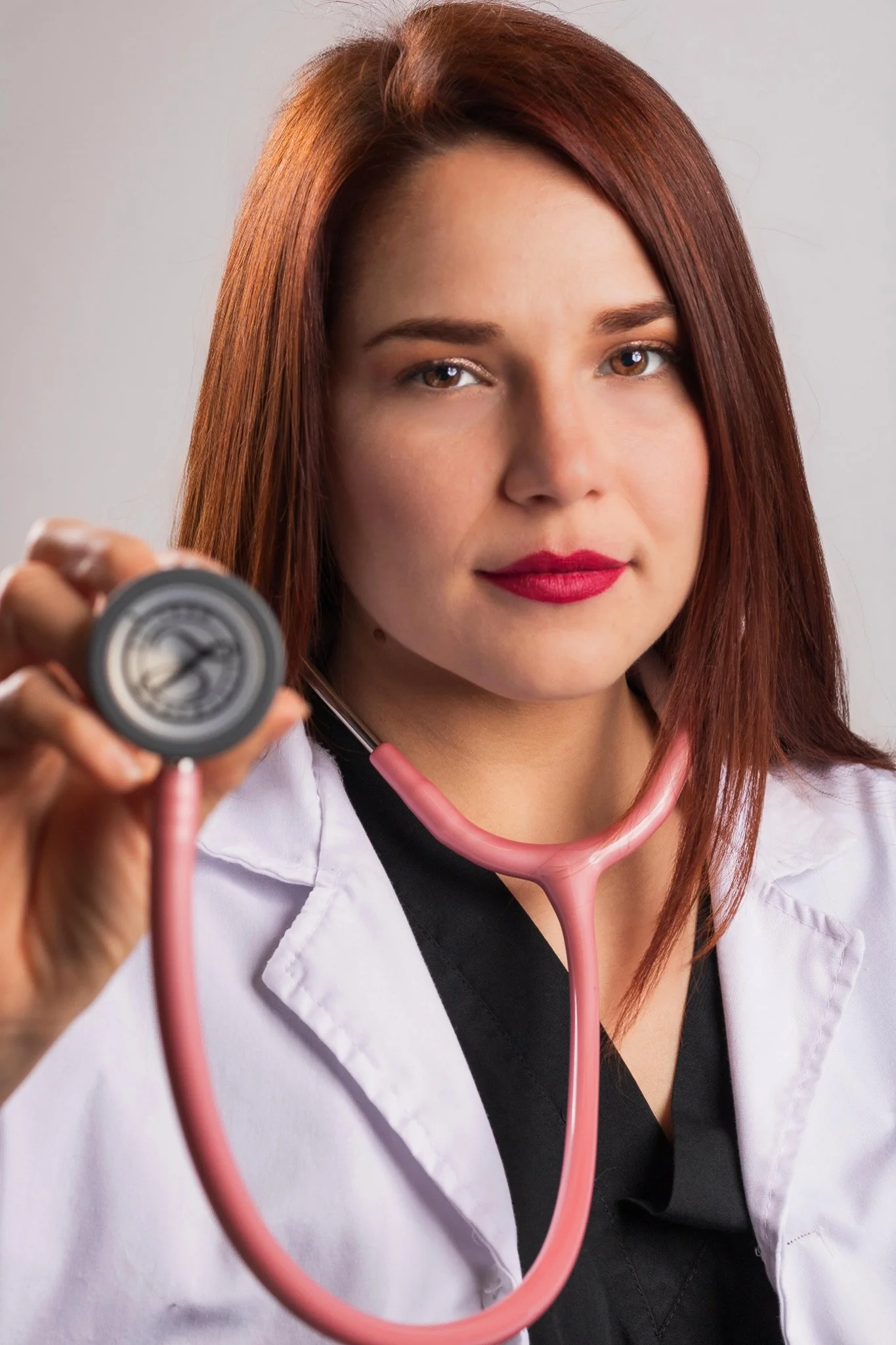 Médica con bata blanca y estetoscopio rosa, sosteniendo un esfigmomanómetro, mirando hacia la cámara.