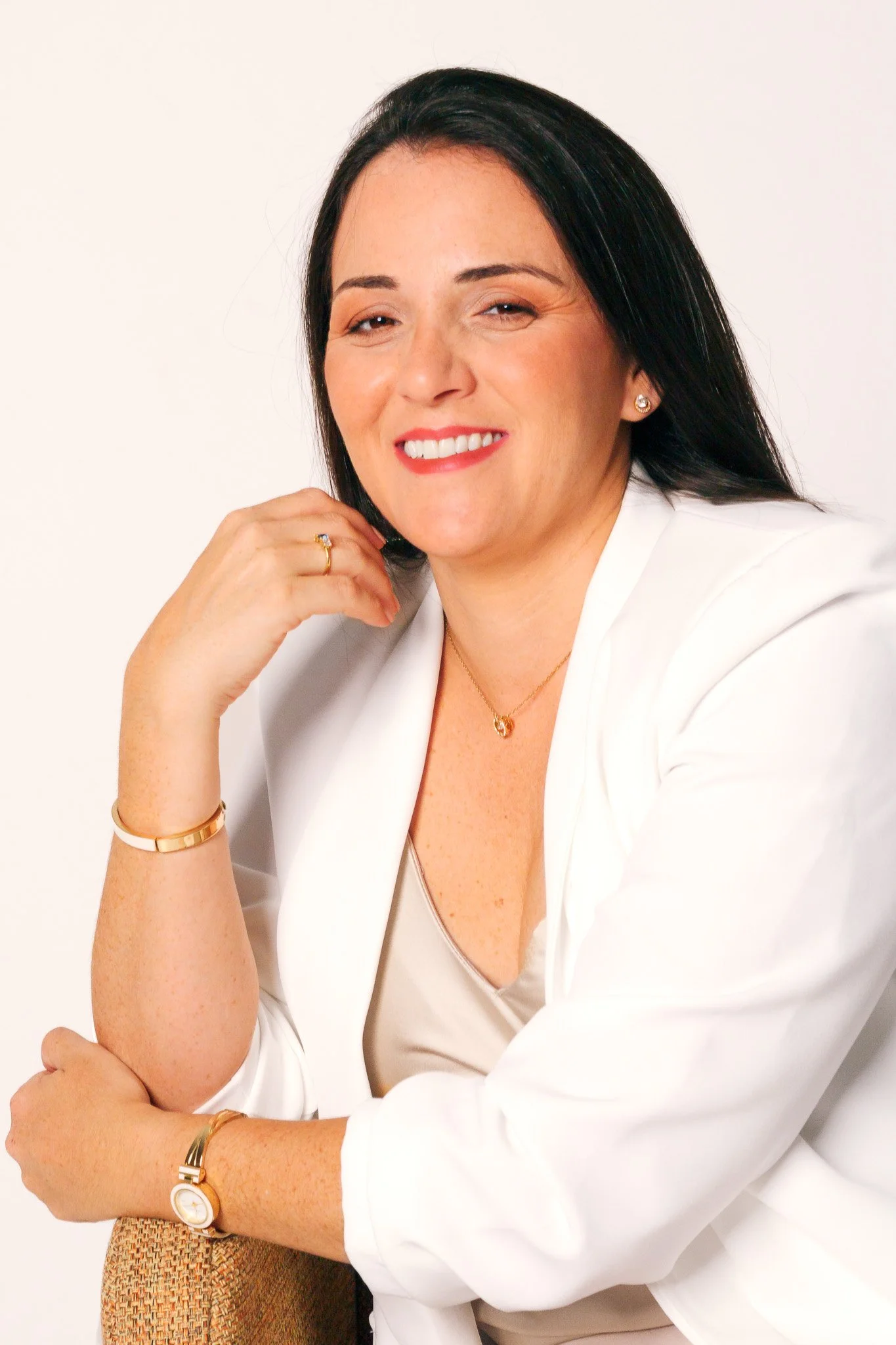 Retrato de una mujer sonriendo, con cabello negro y blusa blanca, posando en un fondo blanco.