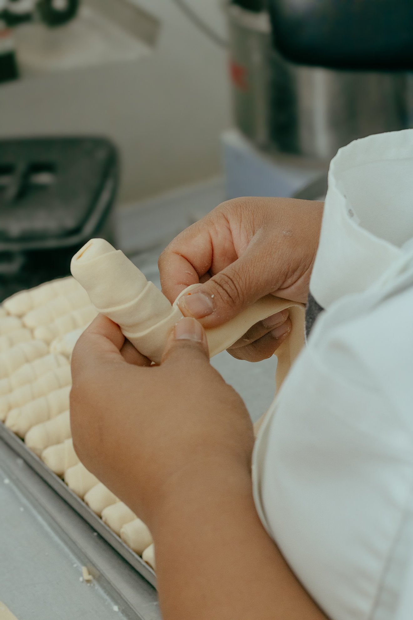 Manos moldeando una pieza de masa para hacer animales de masa en una cocina, con bancas llenas de figuras terminadas en exhibición.