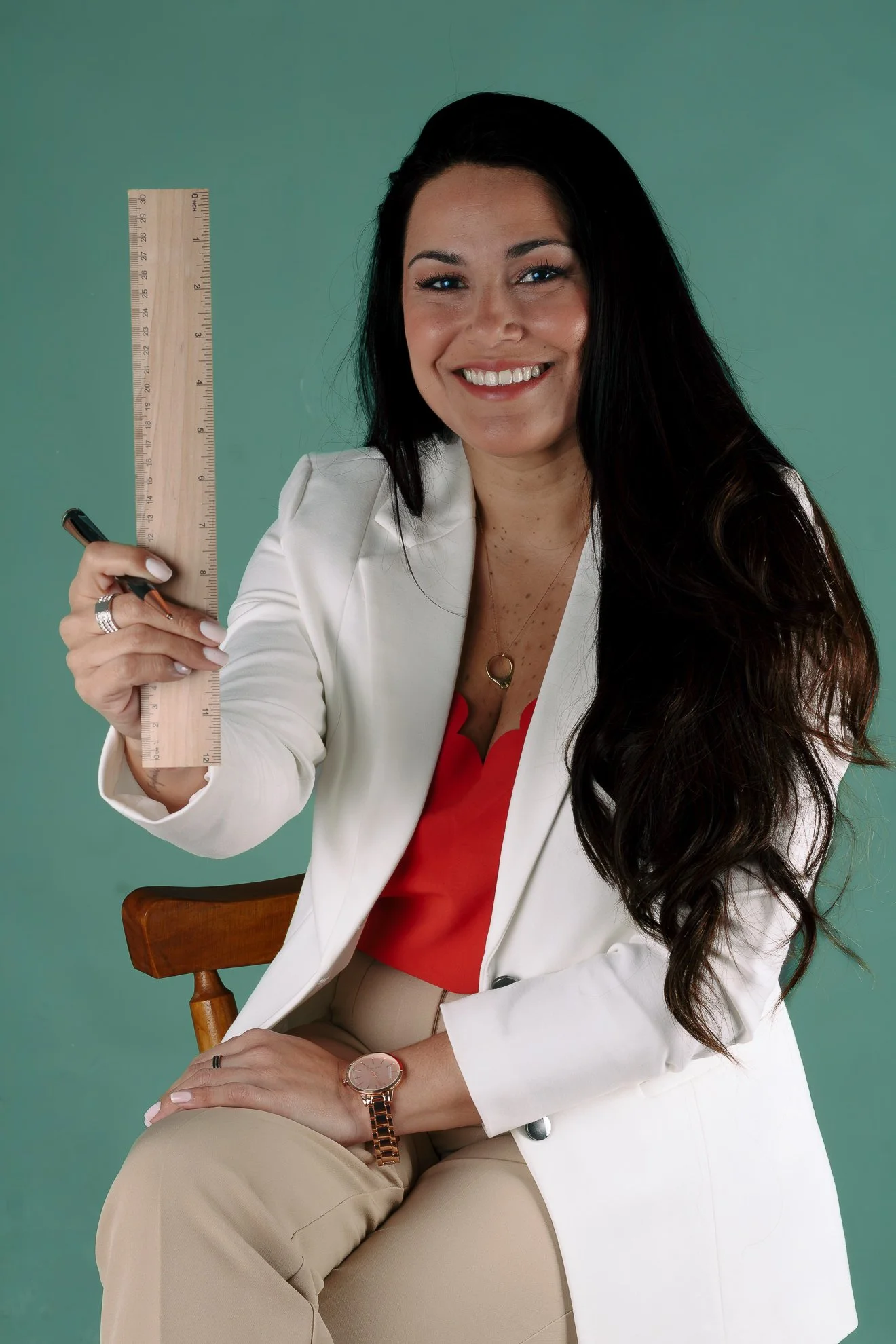 Mujer sonriendo, usando blazer blanco, sosteniendo una regla y un bolígrafo, en fondo verde.