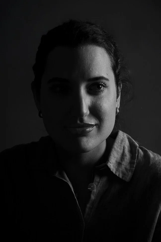 Retrato de una mujer con expresión en color negro y blanco, con un lado de la cara en sombra, vestido con una camisa de mezclilla y pendiente en la oreja.