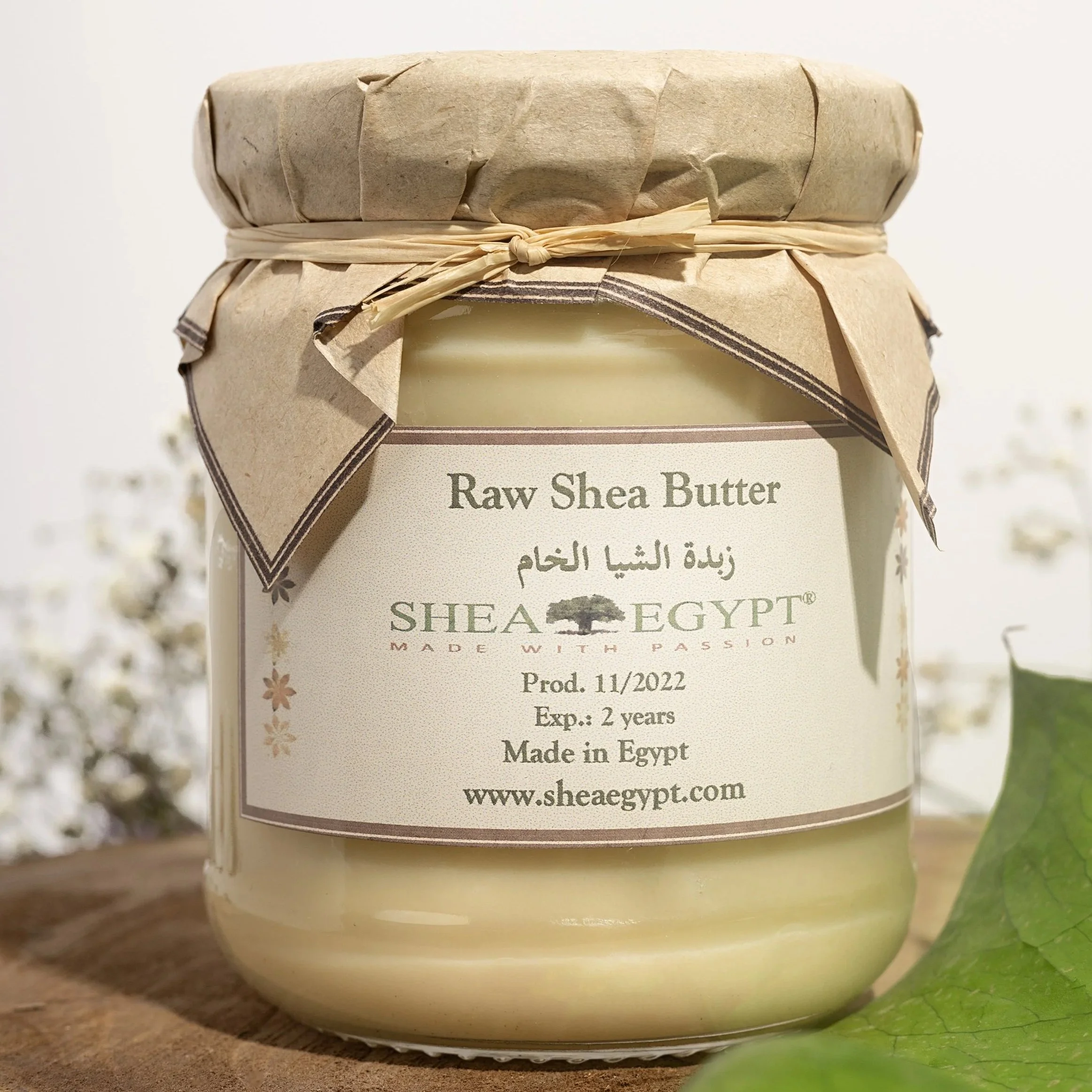 A jar of Raw Shea Butter with a brown paper and twine cover and a label indicating it is made in Egypt by Shea Egypt, with details about production and expiration.