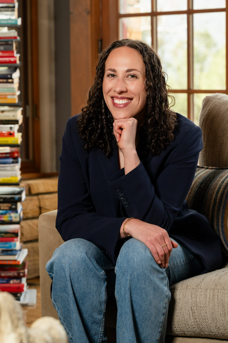 Natalie Youssef, performance coach, sitting in a cozy coaching space with a bookshelf in the background