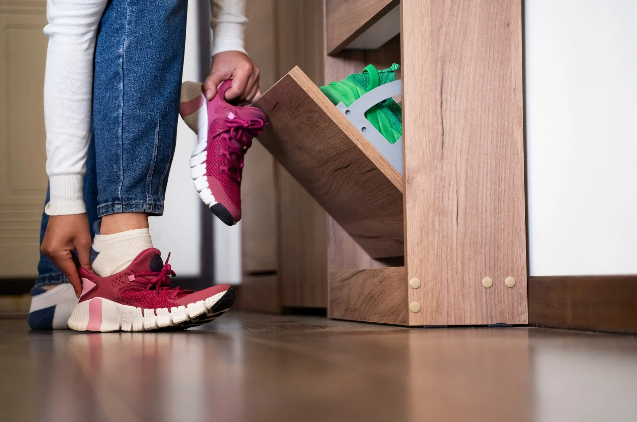 Person putting on pink athletic shoes in front of a shoe cabinet with green shoes stored inside.