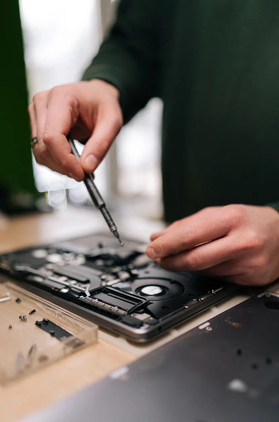 Person repairing a smartphone using a small screwdriver on a workbench with small parts around.