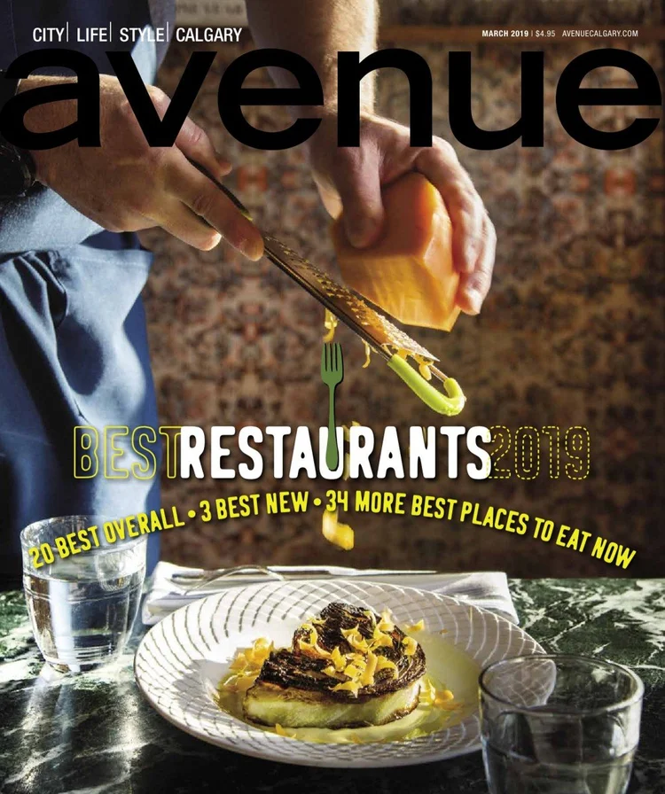 Cover of a magazine titled 'Avenue' featuring a person grating cheese over a plated dish of pasta or risotto, with glasses of water on a marble table.