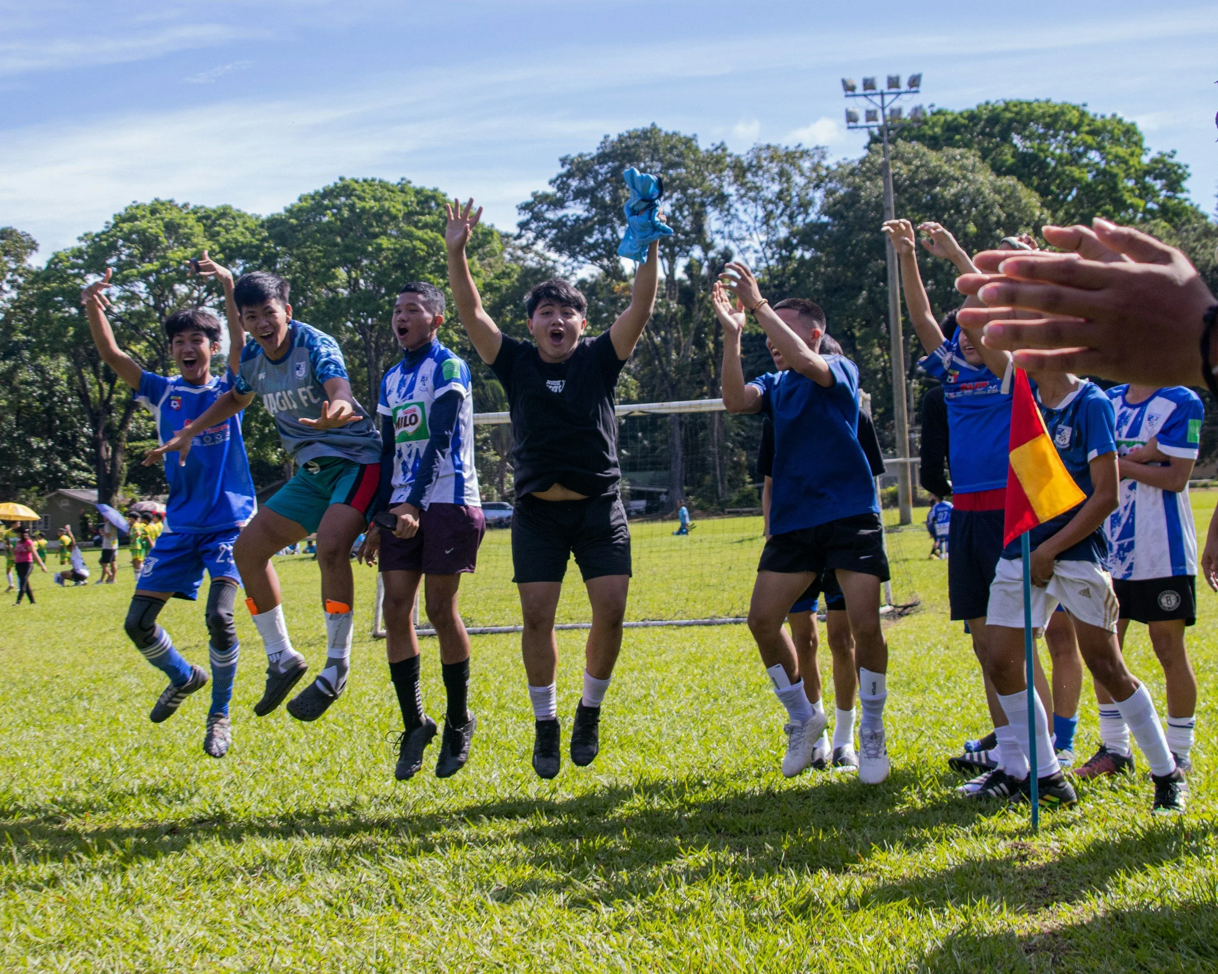 A group of young boys in soccer uniforms celebrating and jumping in the air on a soccer field during a game or practice.
