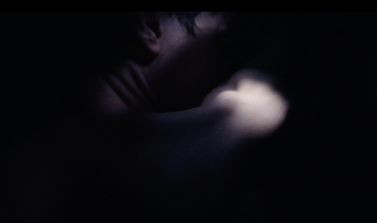 Person sitting with head bowed, arm resting on knee, in a dark environment, illuminated softly from above.