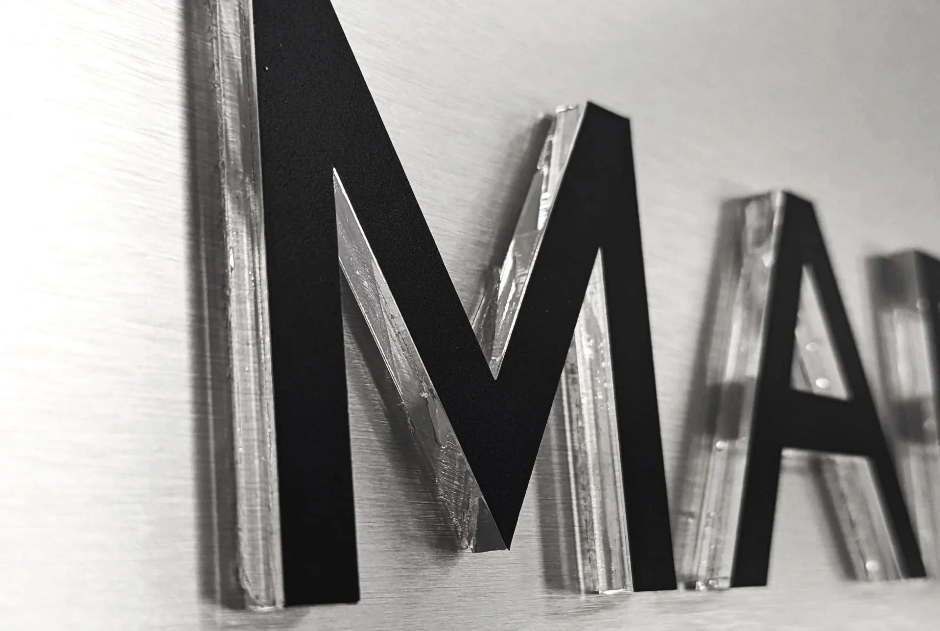 Close-up of black and silver 3D letters on a wall, spelling out 'M'.}