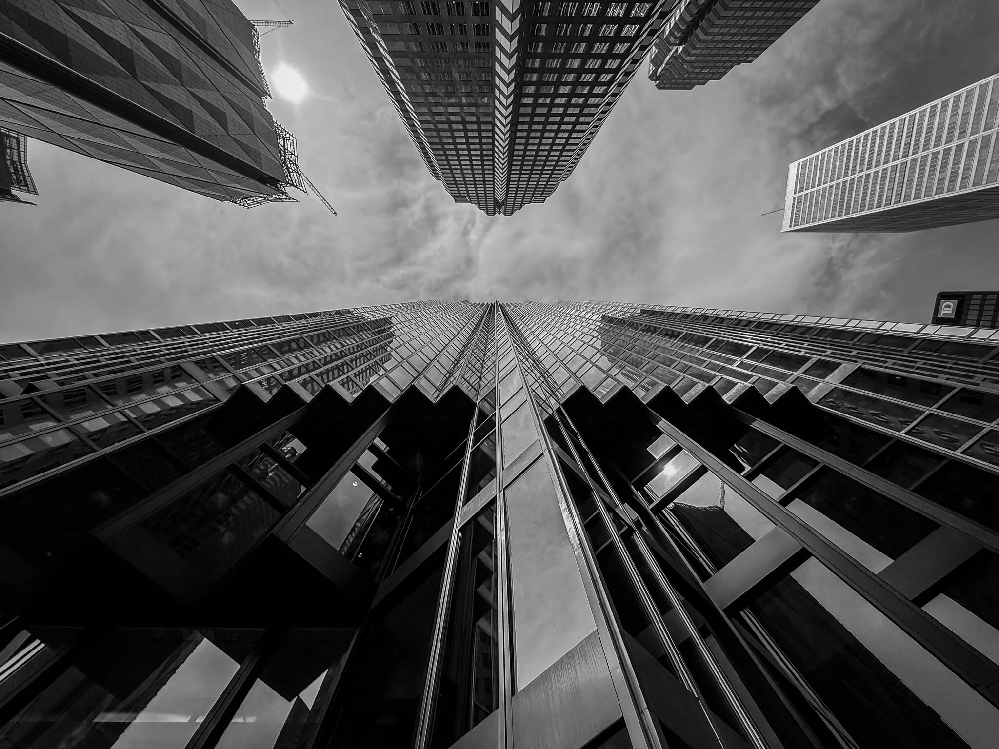 Low-angle black and white photo of tall skyscrapers with glass facades in a city.