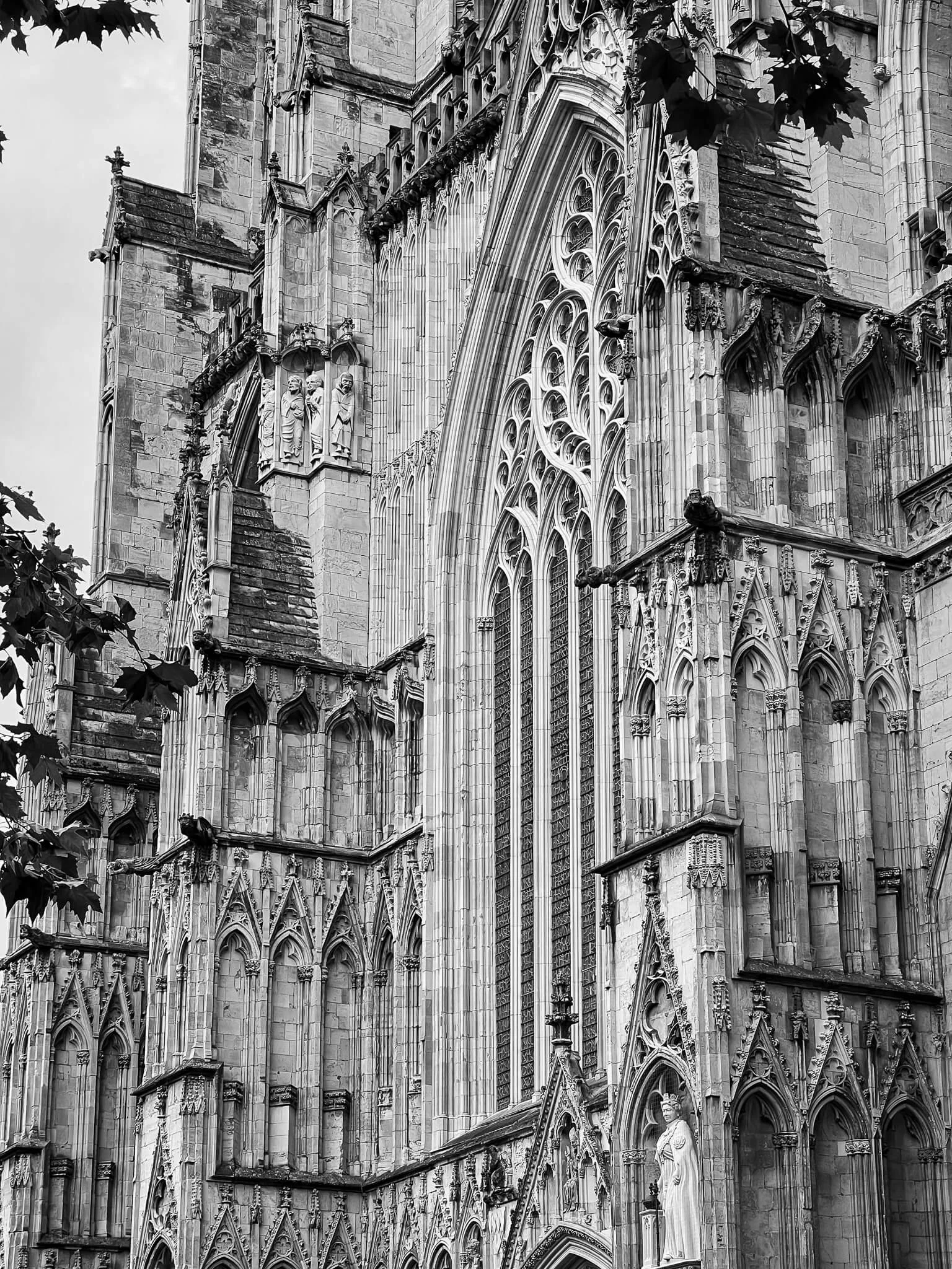 Black and white photo of a Gothic cathedral with intricate stone carvings, pointed arches, stained glass windows, and statues on its facade.