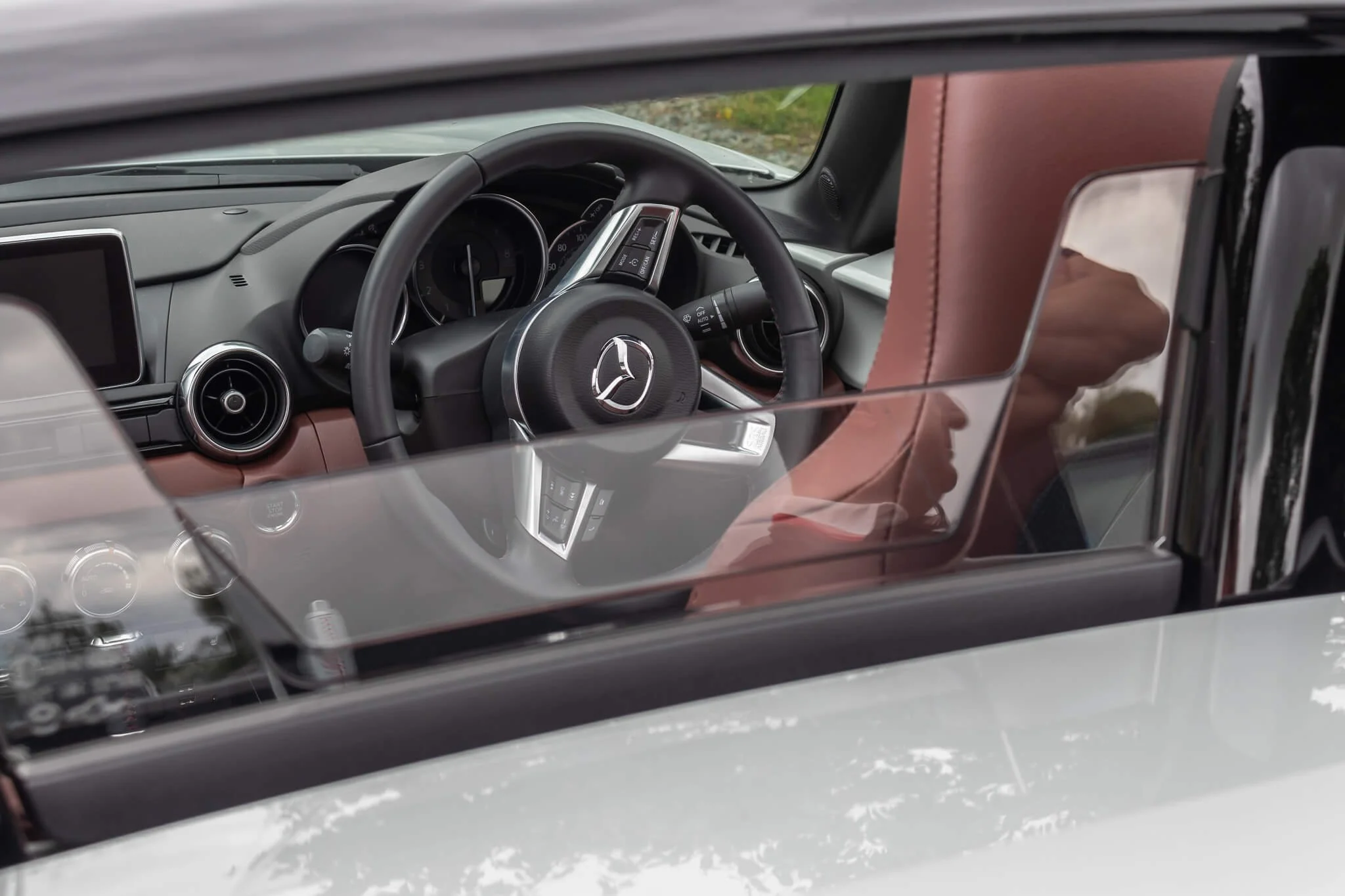 View of the interior of a Mercedes-Benz car, seen through the front windshield, including the steering wheel with the Mercedes-Benz logo, dashboard, and brown leather interior, with a partial view of the outside environment.