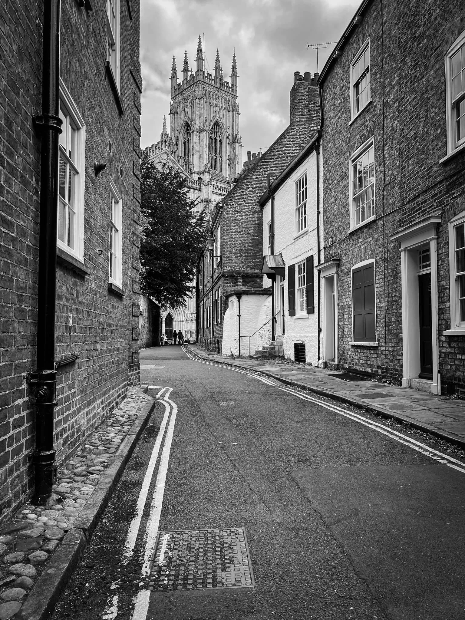 A narrow street in a city with brick buildings on either side and a large Gothic-style cathedral visible in the background.