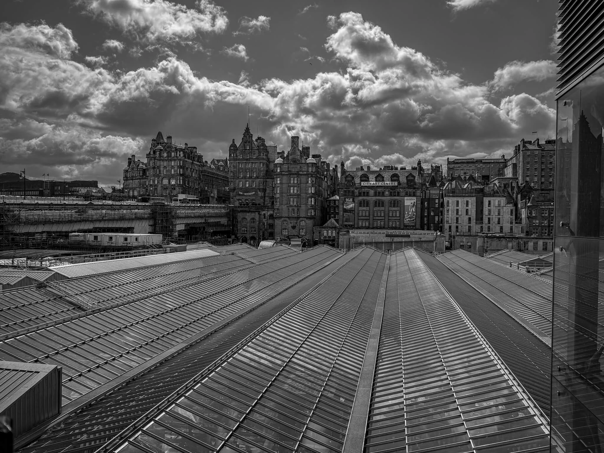 Black and white photo of city rooftops and historic building skyline with cloudy sky in background.