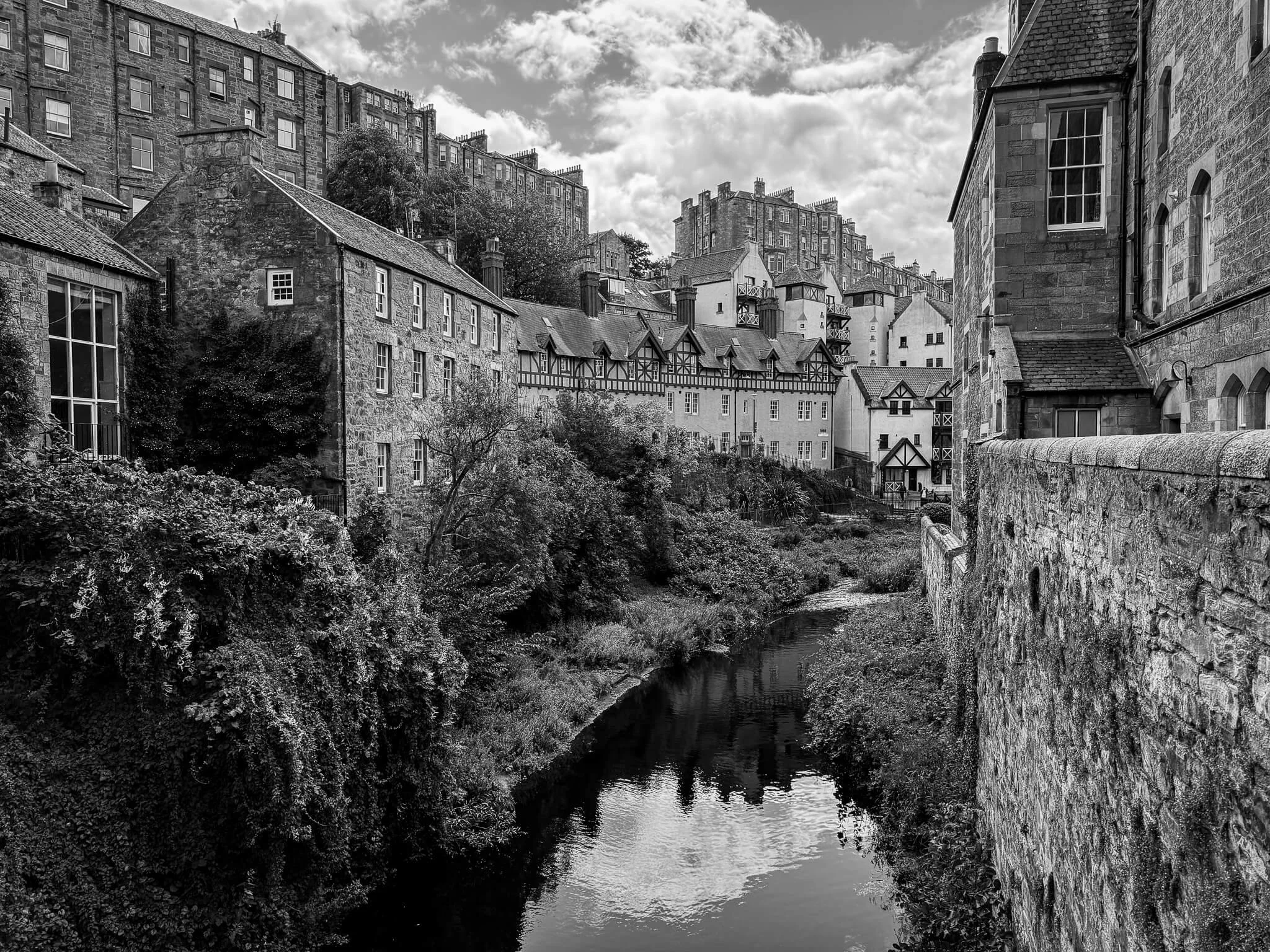 Black and white photo of a quaint town with historic buildings built along a small river or canal, with a cloudy sky overhead.