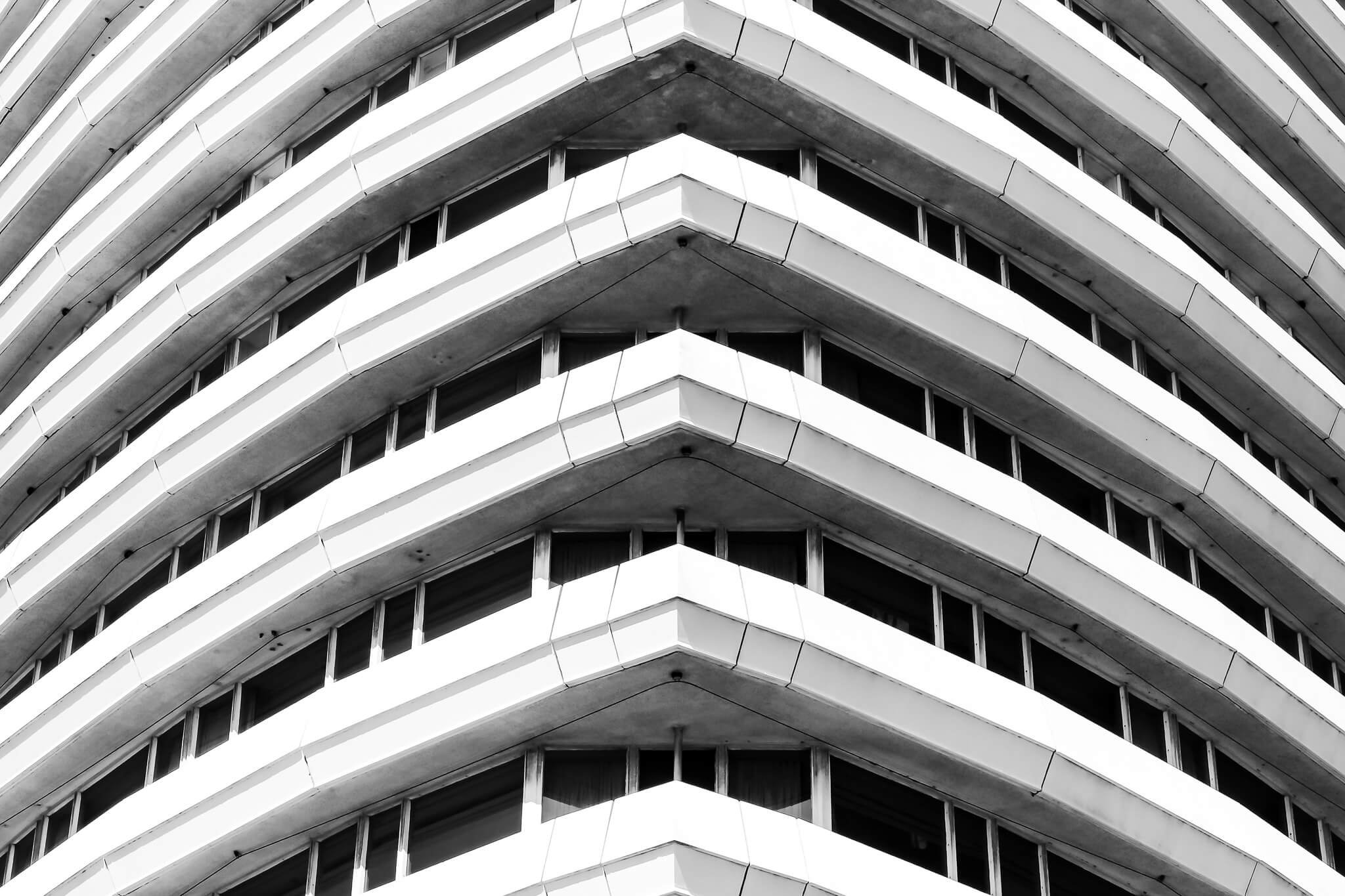 Close-up view of a modern, multi-story building with curved balconies and horizontal lines, in black and white.