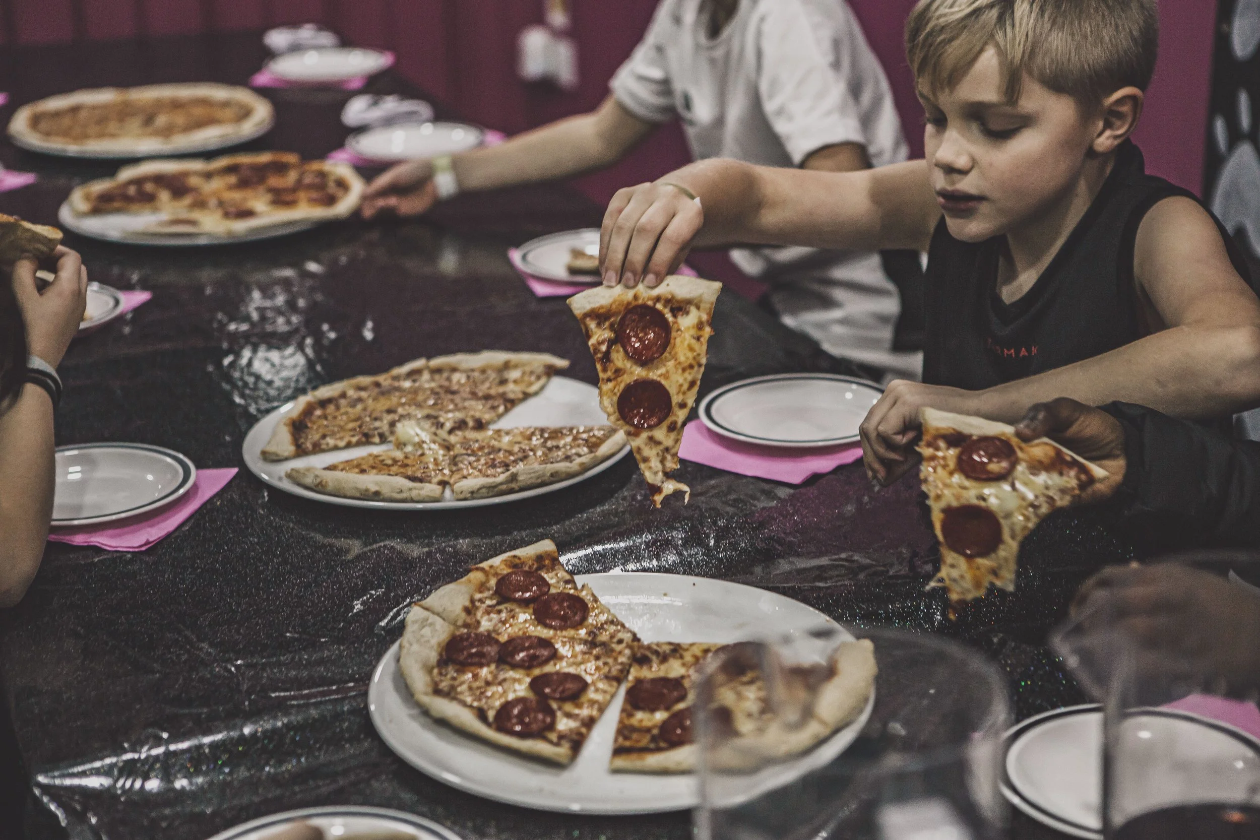 Children sitting at a table eating pizza with pepperoni slices.