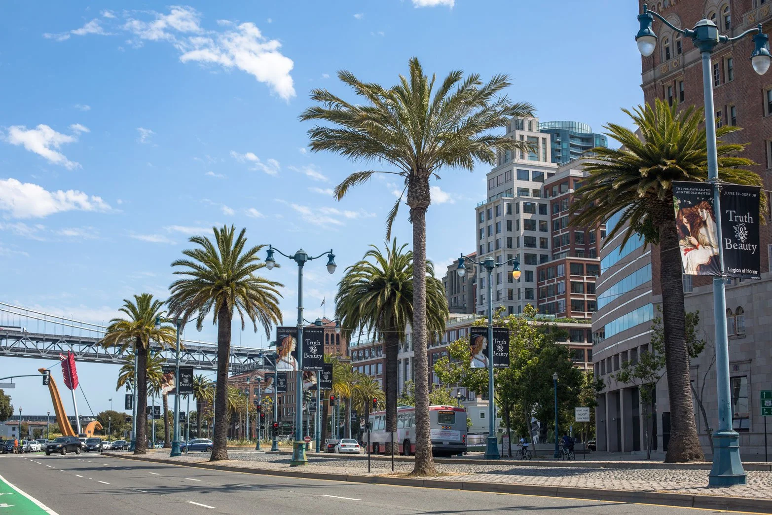 Street scene with palm trees, tall buildings, and banners that read 'Truth & Beauty' in a city with a clear blue sky.