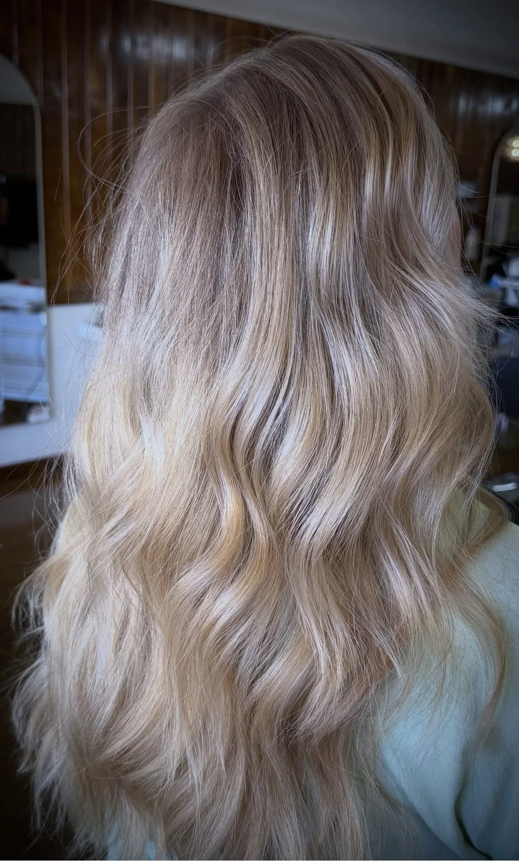 Wavy blonde hair with subtle highlights, viewed from the back indoors.