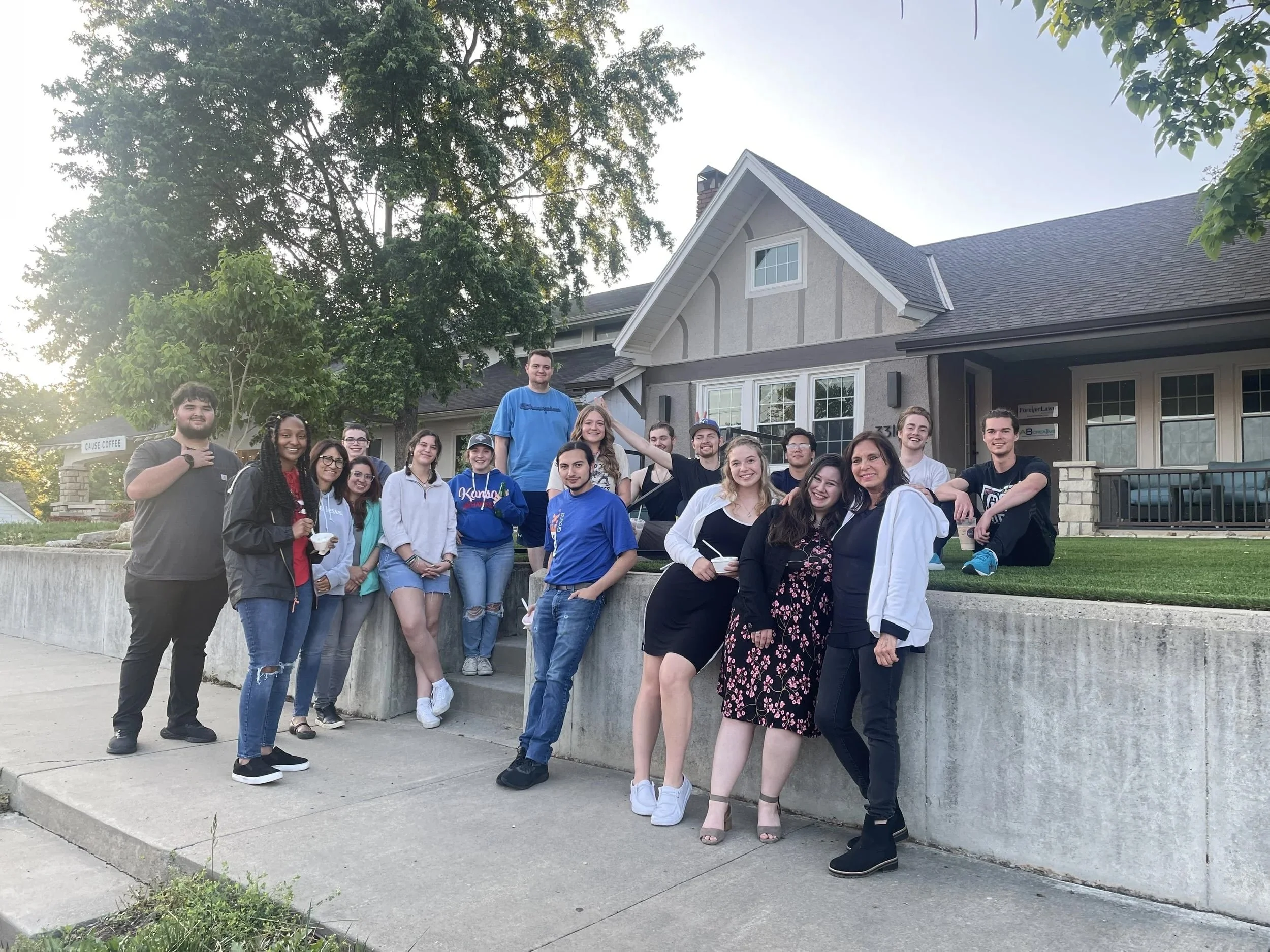 A group of young adults poses and smiles together outside a house on a sunny day, ready for a Fireside gathering.