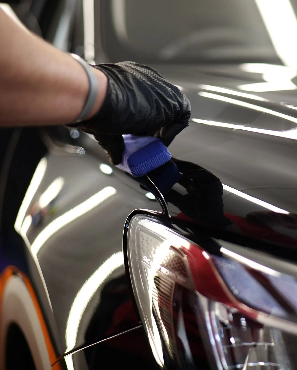 A person wearing black gloves polishing or detailing a black car's exterior.