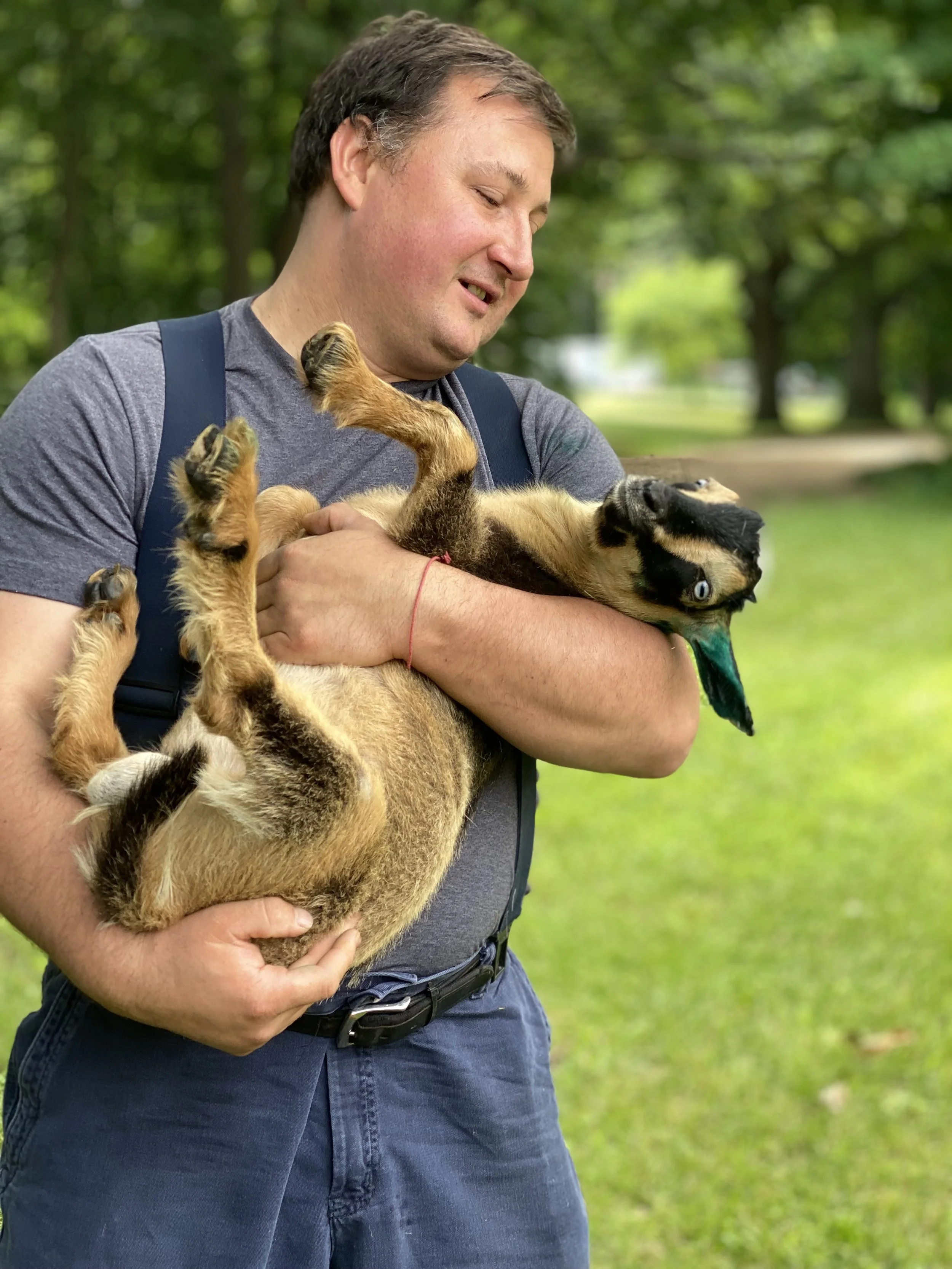 A man holding a playful puppy outdoors with green trees in the background.