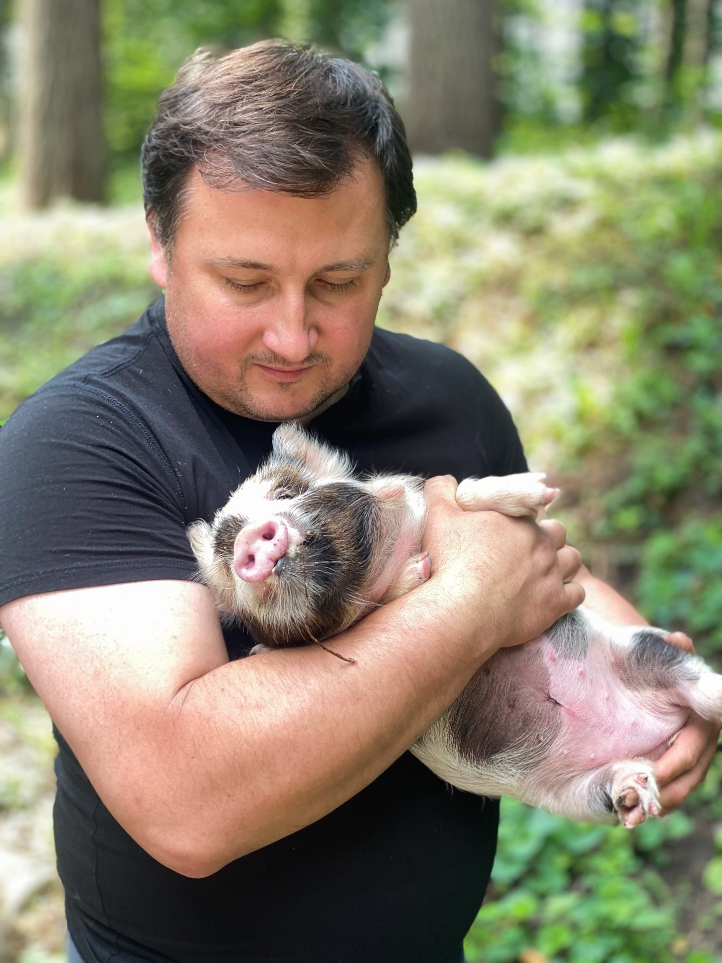 A man holding a piglet in a forested setting.