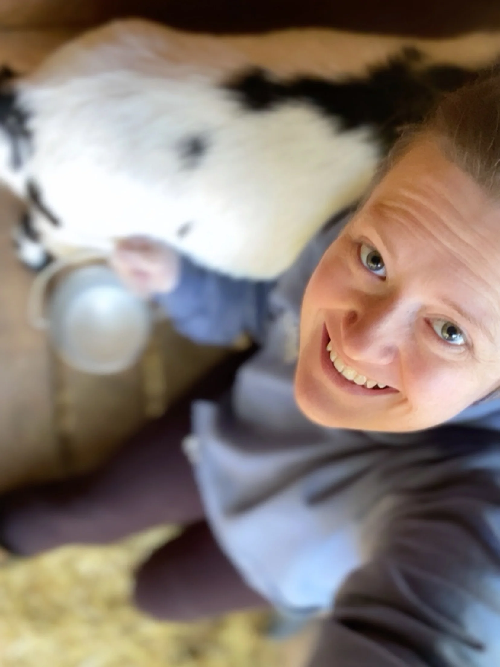 Close-up of a laughing woman with piercing green eyes, visible teeth, and wearing a striped shirt, with a dog partially in the frame.