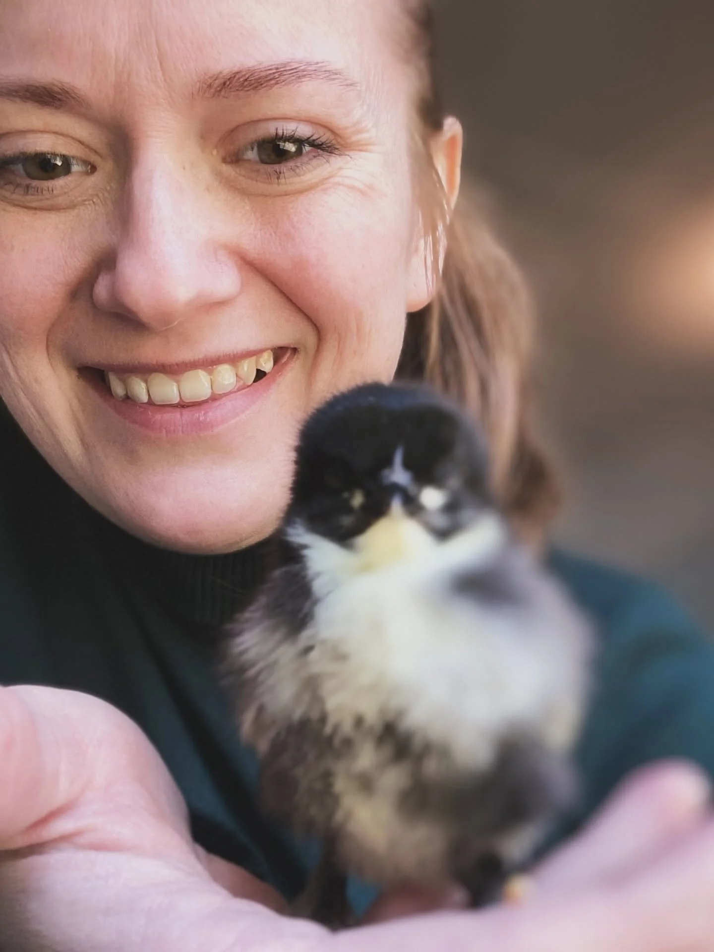 A close-up of a woman smiling with a small black and white chick near her face.