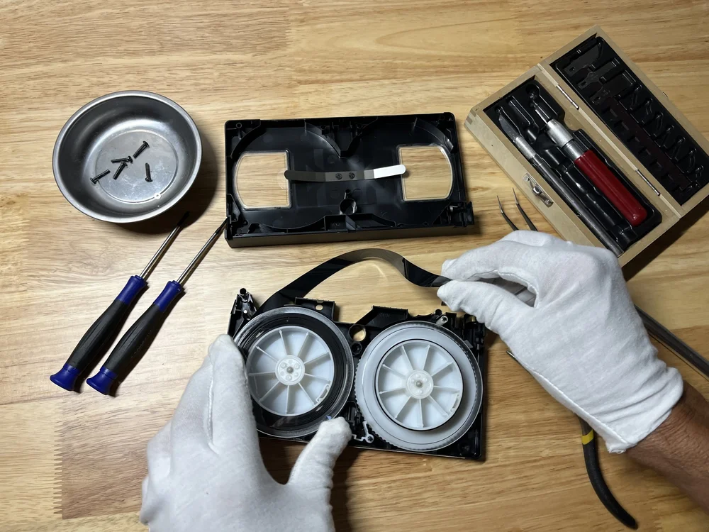Gloved hands working on an opened videotape beside repair tools at Coppolo Studios