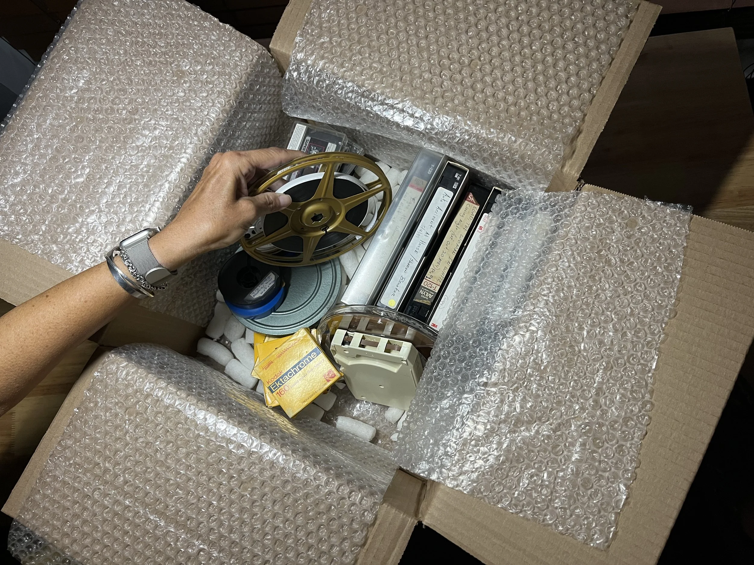 Open cardboard box filled with various vintage electronic items, books, and bubble wrap for protection.