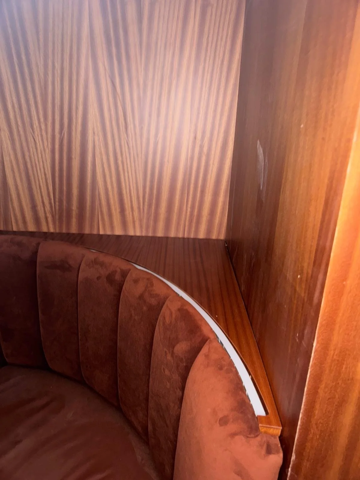 Close-up of a wooden wall with a curved, upholstered seat in a reddish-brown fabric, part of a vintage interior furniture set.