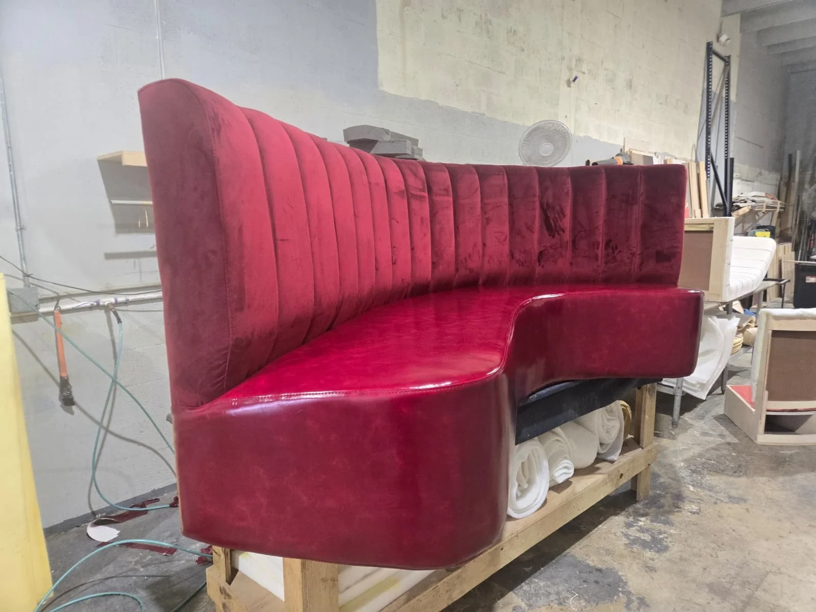 Red upholstered booth seat with vertical channels, placed on a wooden pallet in a workshop or storage area.