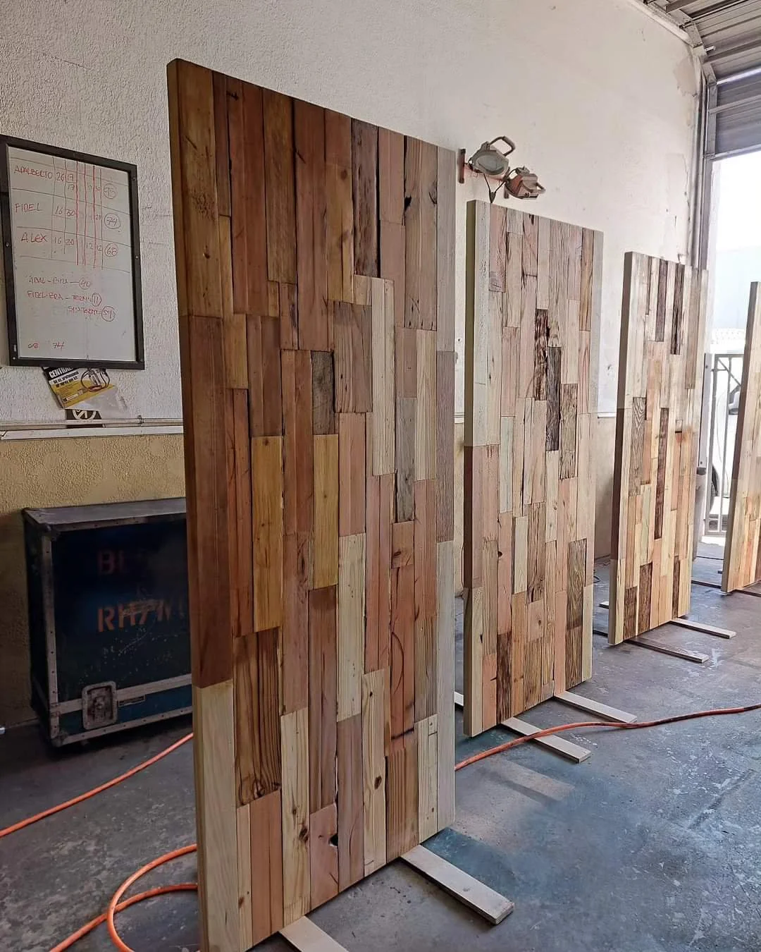Wooden panels with assorted tones arranged vertically, standing on a concrete floor in a workshop or construction area.