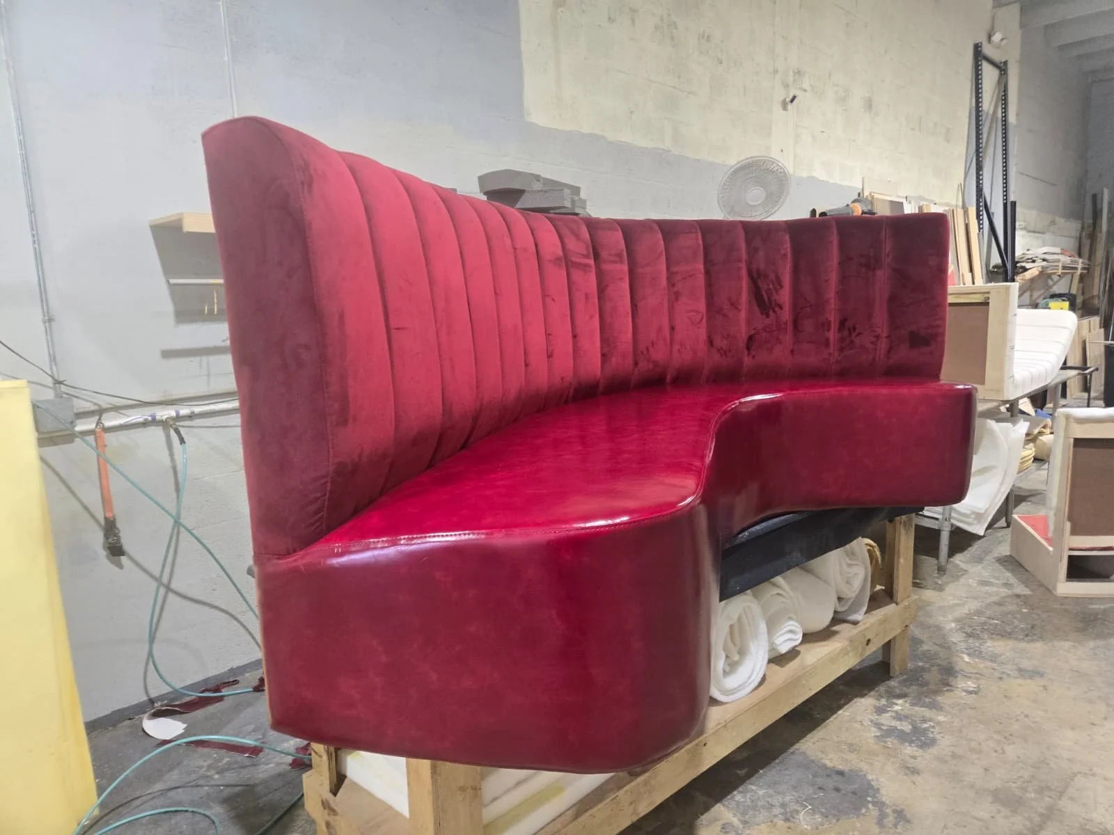 A red upholstered booth with vertical tufting in a workshop or warehouse setting.