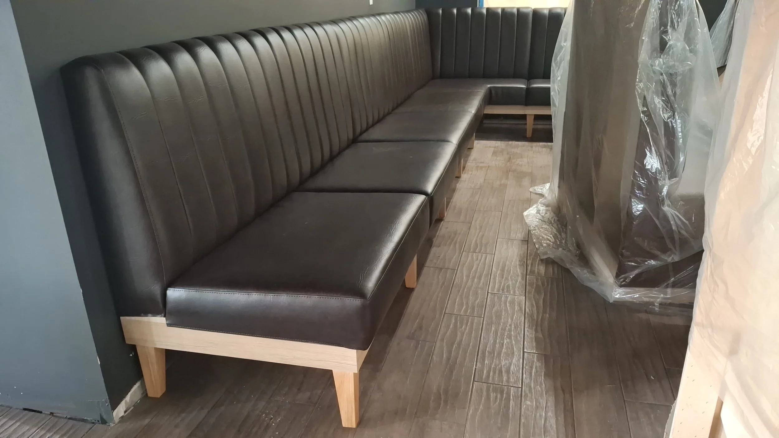 A black leather booth seating with a wooden frame and legs situated on brown tile flooring.