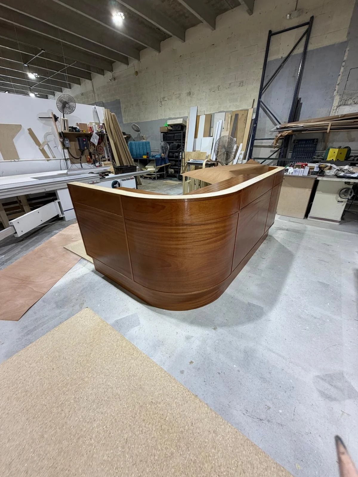 A woodworking workshop with a curved wooden piece in the center, surrounded by tools, woodworking equipment, and materials.
