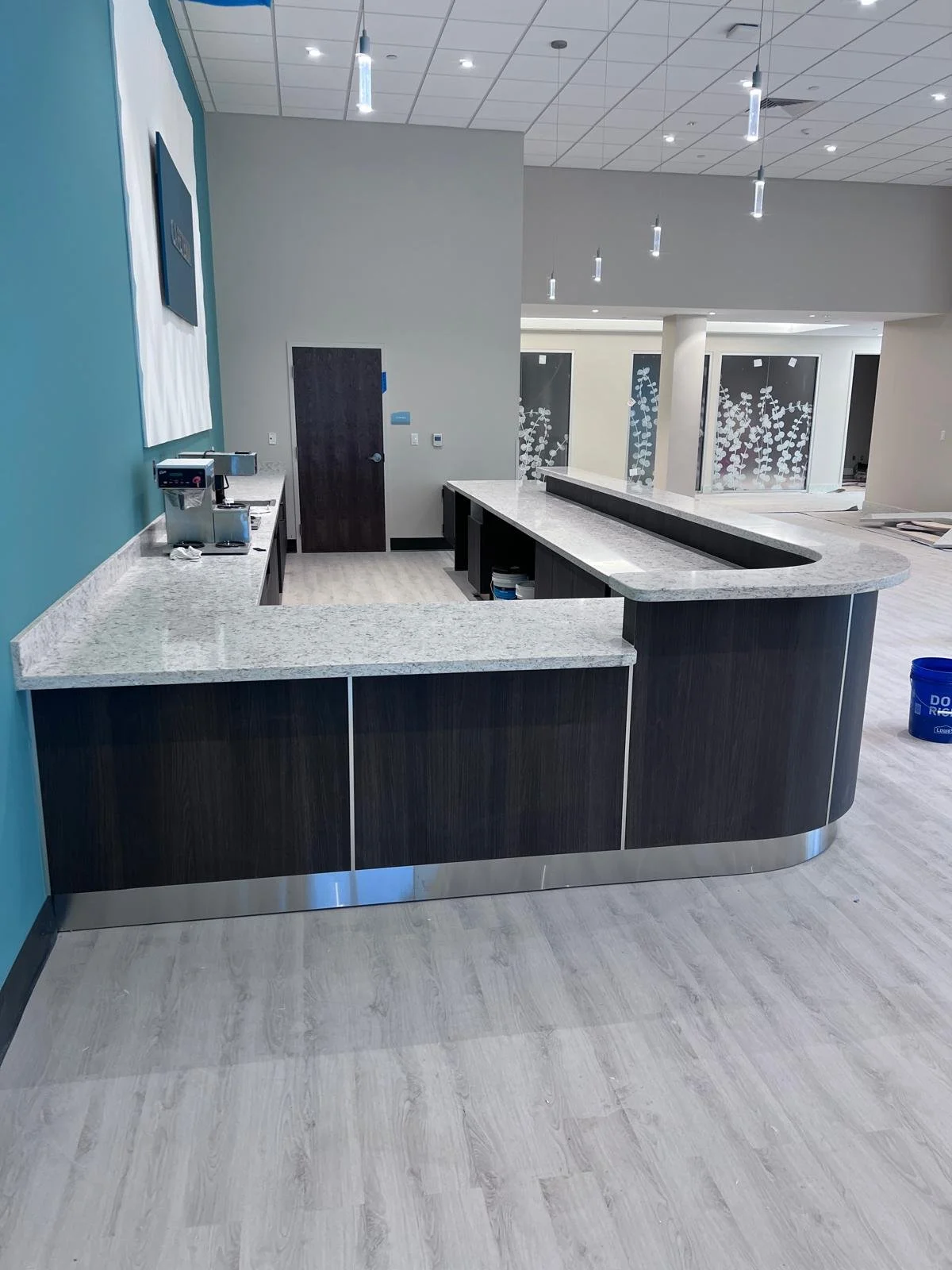 Empty modern café or reception area with a curved granite bar counter, blue accent wall, and decorative window coverings with white floral patterns.