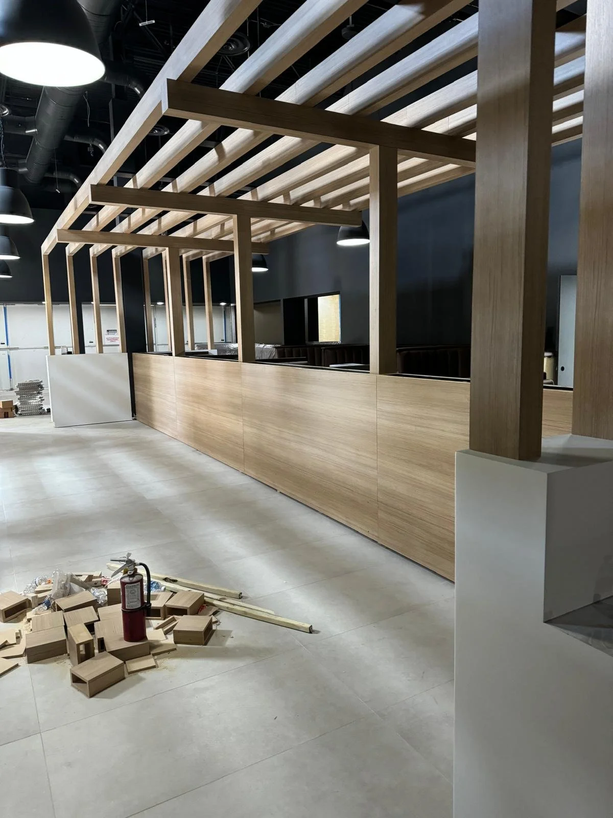 Interior under construction with wooden framework, light wood paneling, construction tools, debris, and a fire extinguisher on the floor.